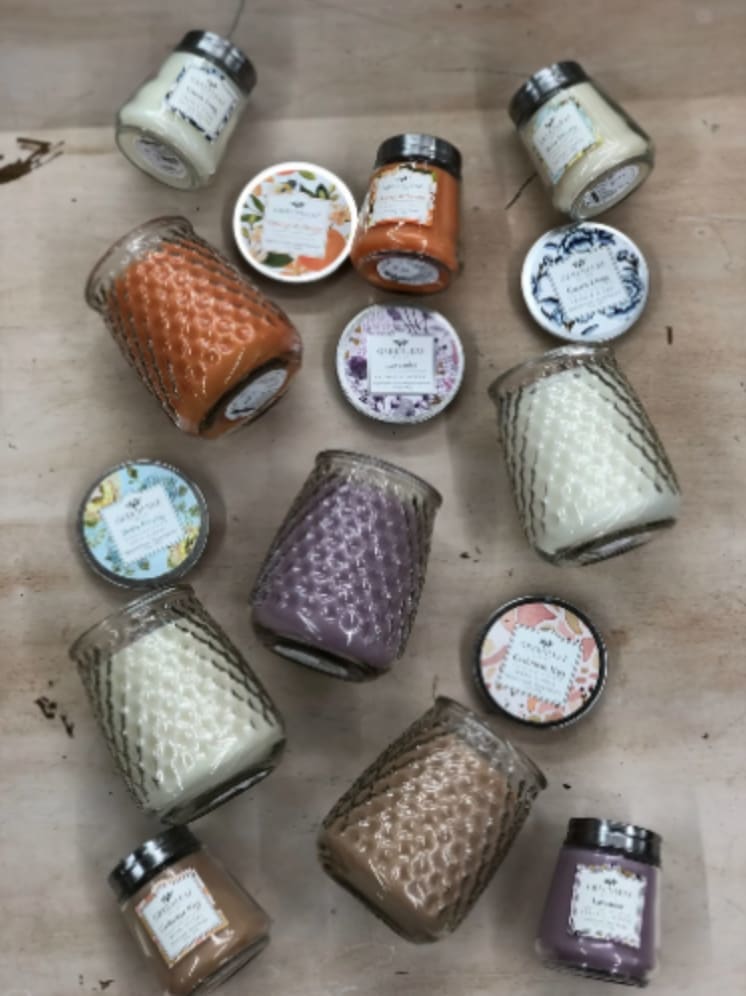 Assorted colored candles in textured glass jars with decorative lids arranged on a wooden surface