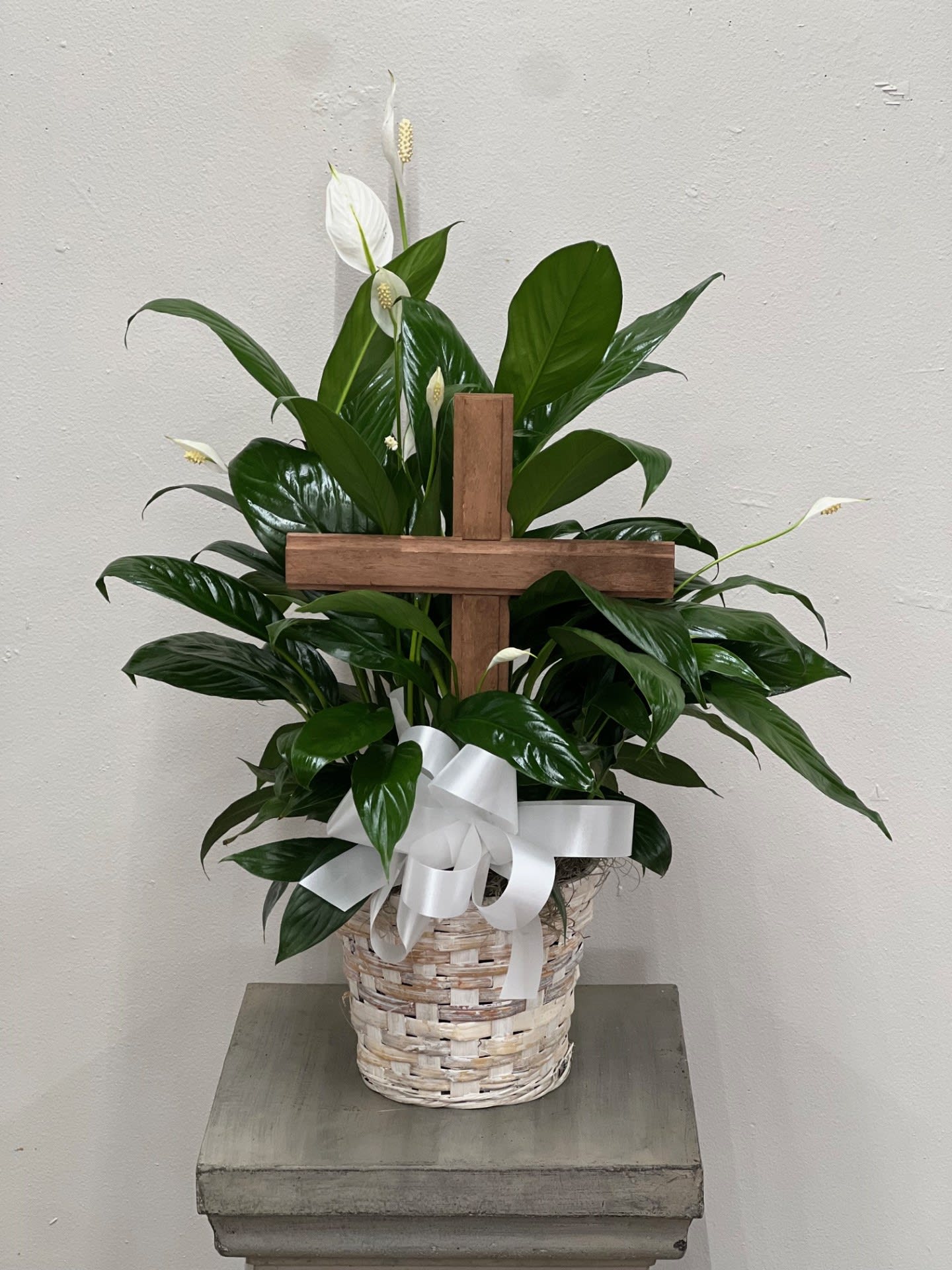 White peace lilies in a wicker basket with a wooden cross and white ribbon