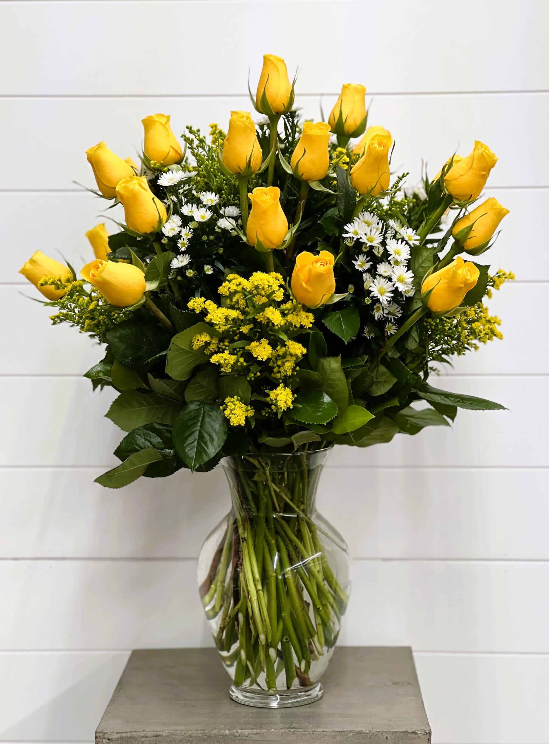 Yellow roses and small white flowers arranged in a clear glass vase