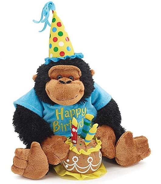 Birthday gorilla plush wearing a party hat and shirt, sitting with a plush cake and candles