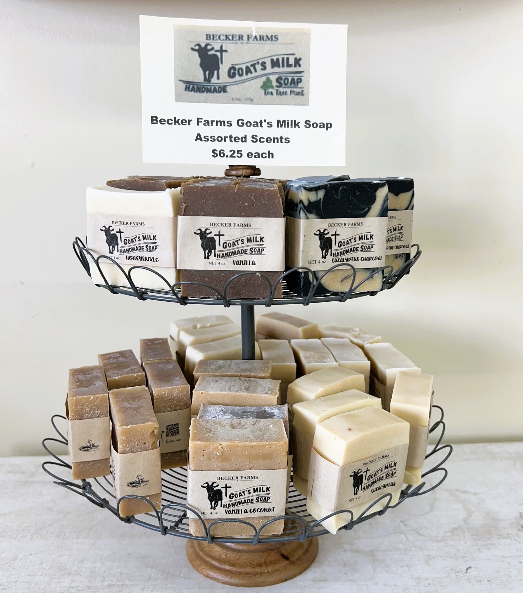 Two-tiered wire stand displaying assorted goat's milk soap bars with beige labels.