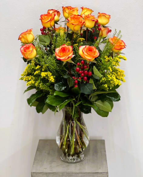 Yellow-orange roses in a clear glass vase with red berries