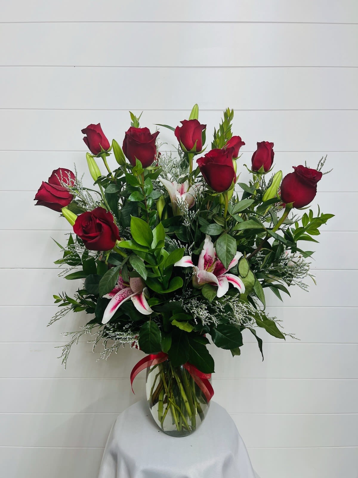 Tall bouquet of red roses and pink lilies in a clear glass vase