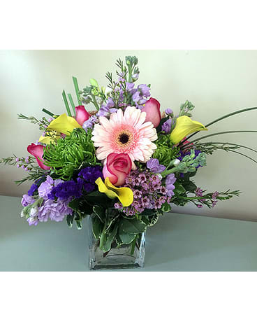 Mixed bouquet with pink gerbera daisies, roses, and purple flowers in a glass vase
