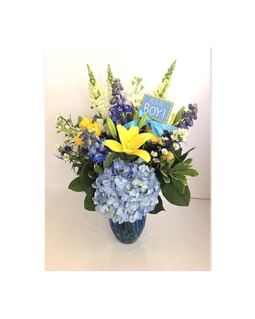 Blue and yellow flower arrangement in a glass vase with a "It's a Boy!" sign