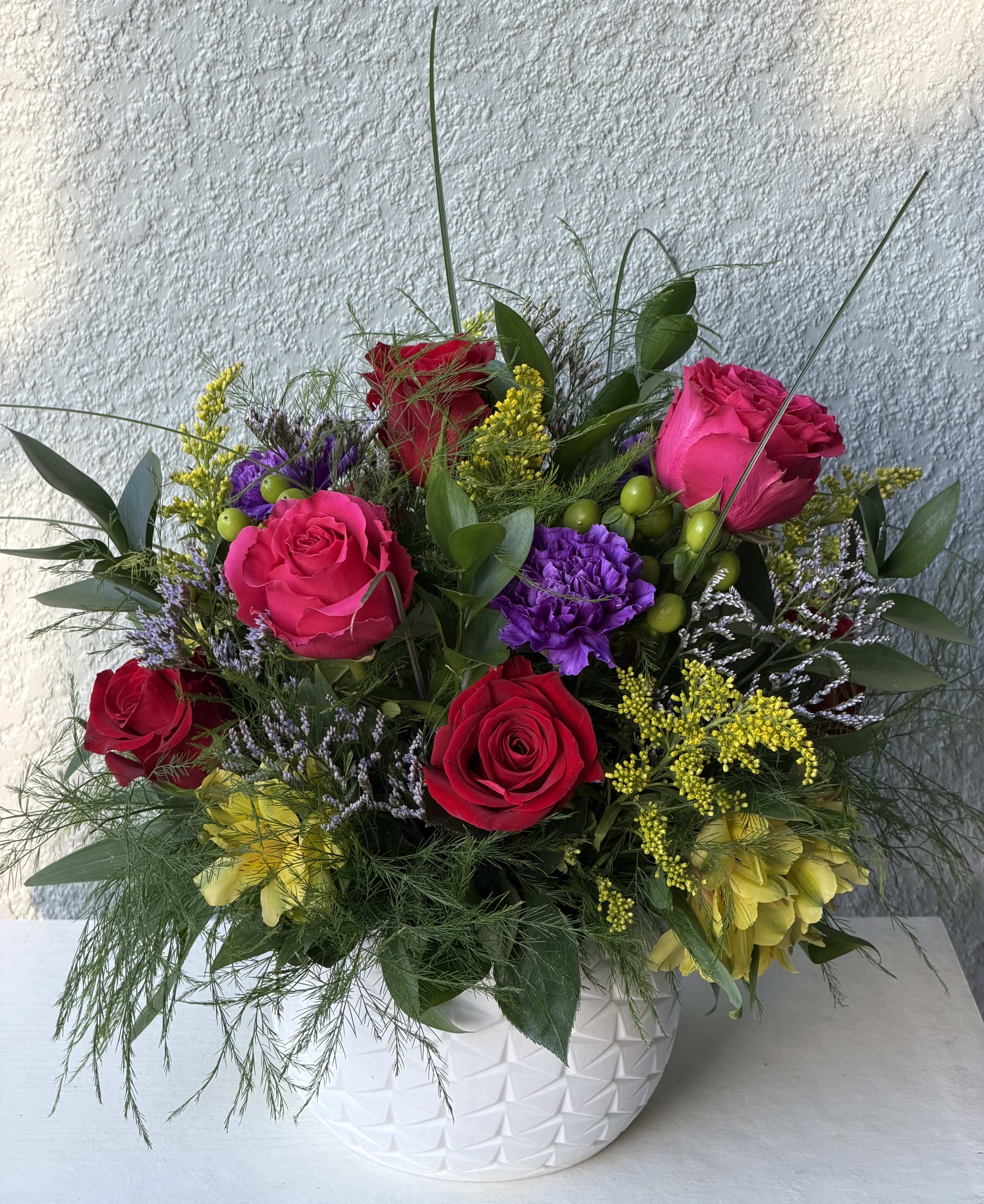 Colorful rose arrangement in a white textured vase with mixed filler flowers
