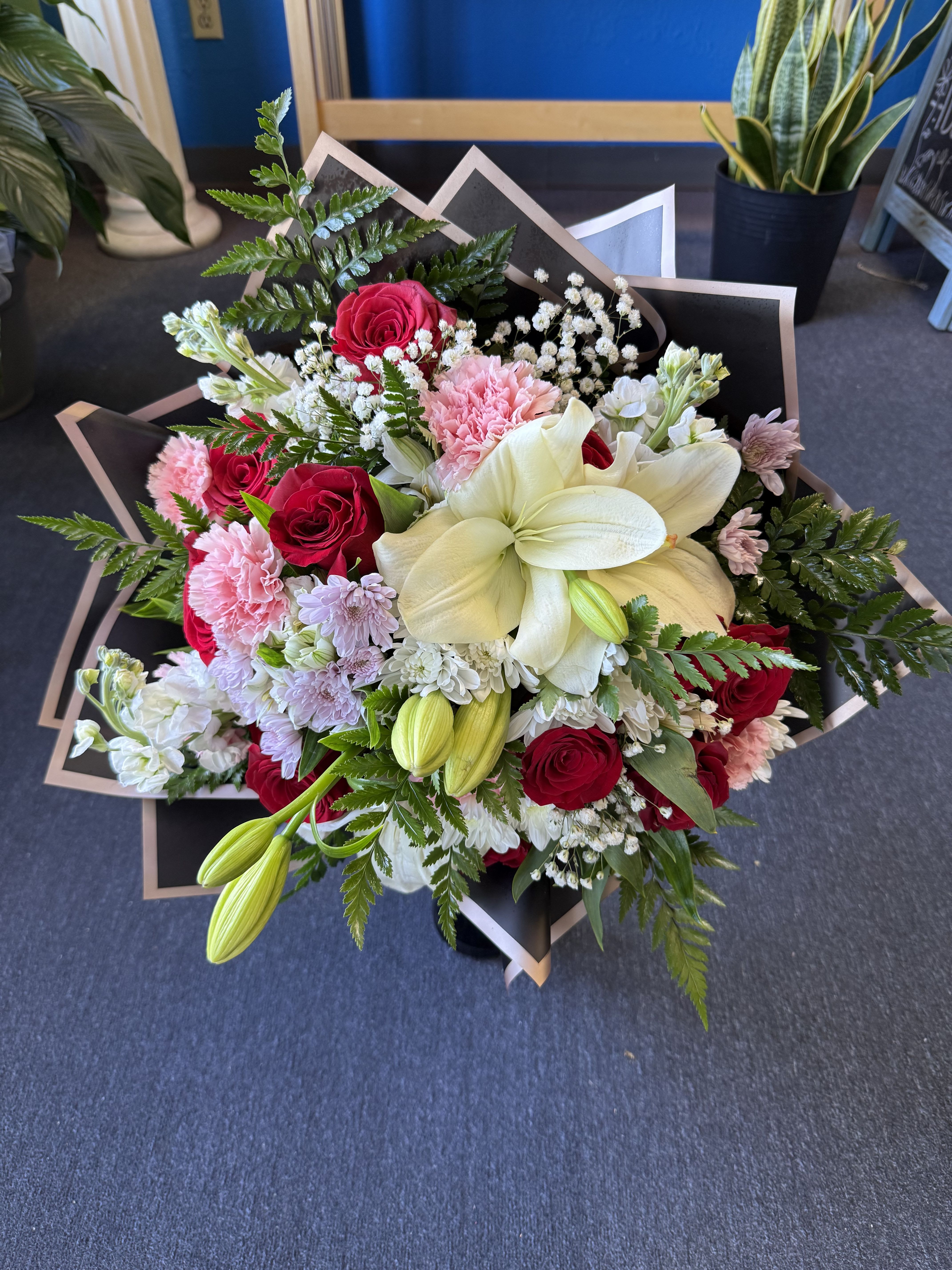 Bouquet of red roses, white lilies, and pink carnations wrapped in black paper