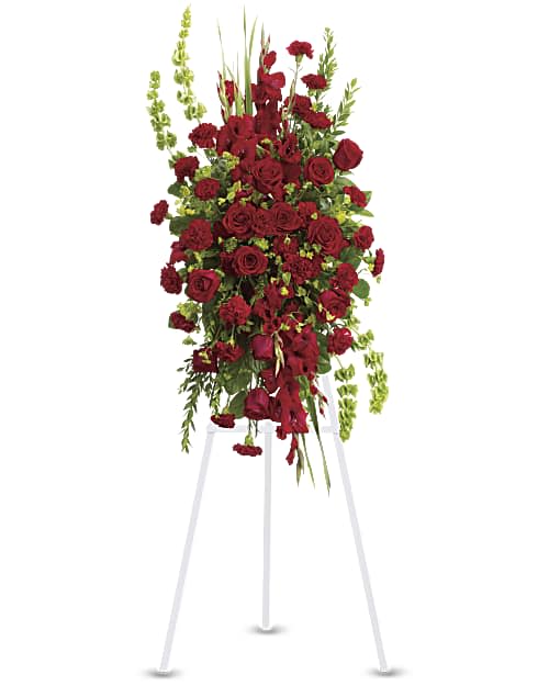 Care and Compassion Spray  - This classic standing spray is thoughtfully arranged with rich red flowers, including elegant roses and carnations, beautifully accented with lush greenery. The deep red tones convey love, respect, and heartfelt remembrance, while the greenery adds balance and fullness to the design. Simple yet meaningful, this spray offers a timeless and respectful tribute suitable for honoring a loved one. 
