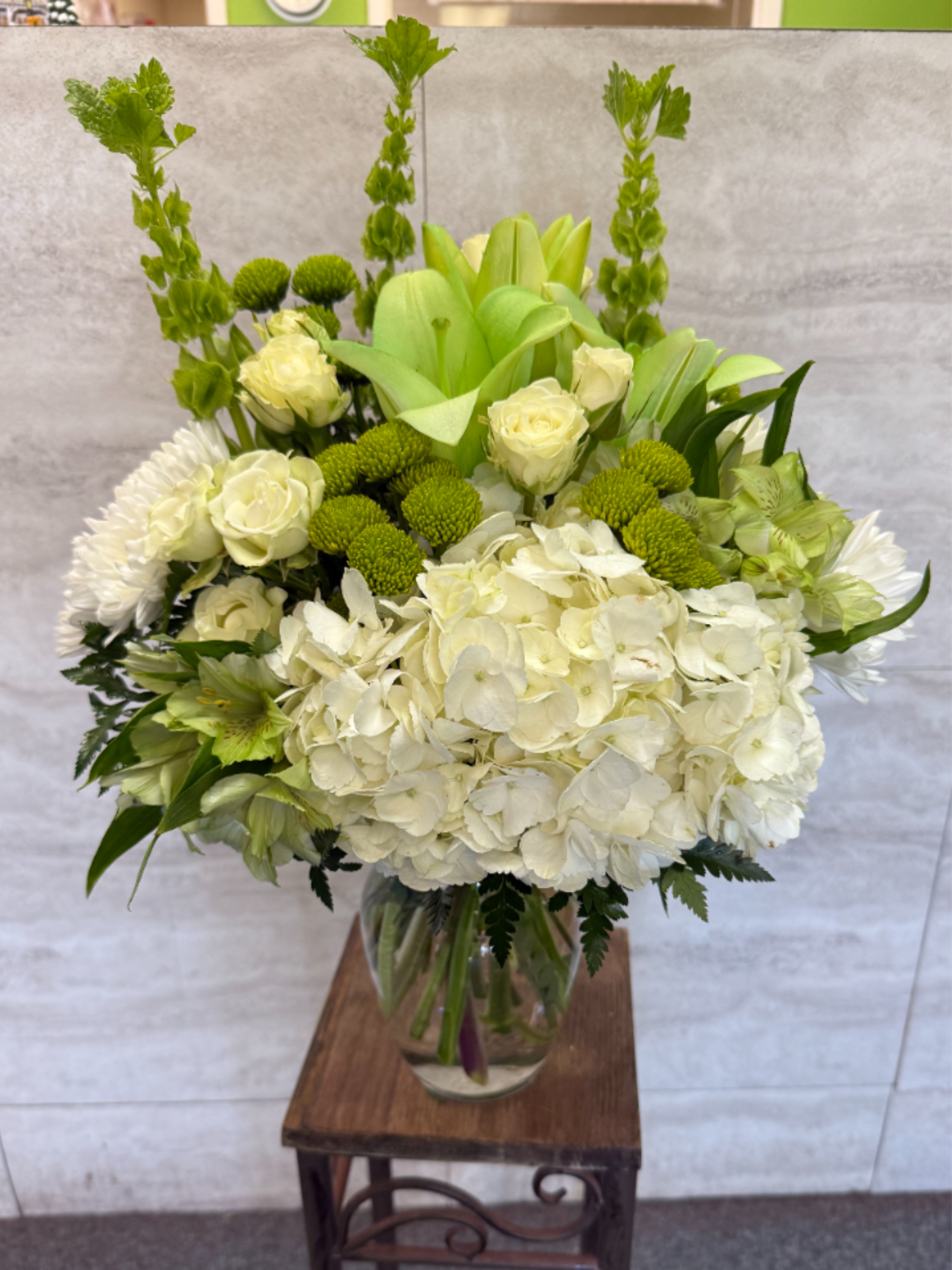 Tall white and green flower arrangement with hydrangeas and roses in a clear glass vase