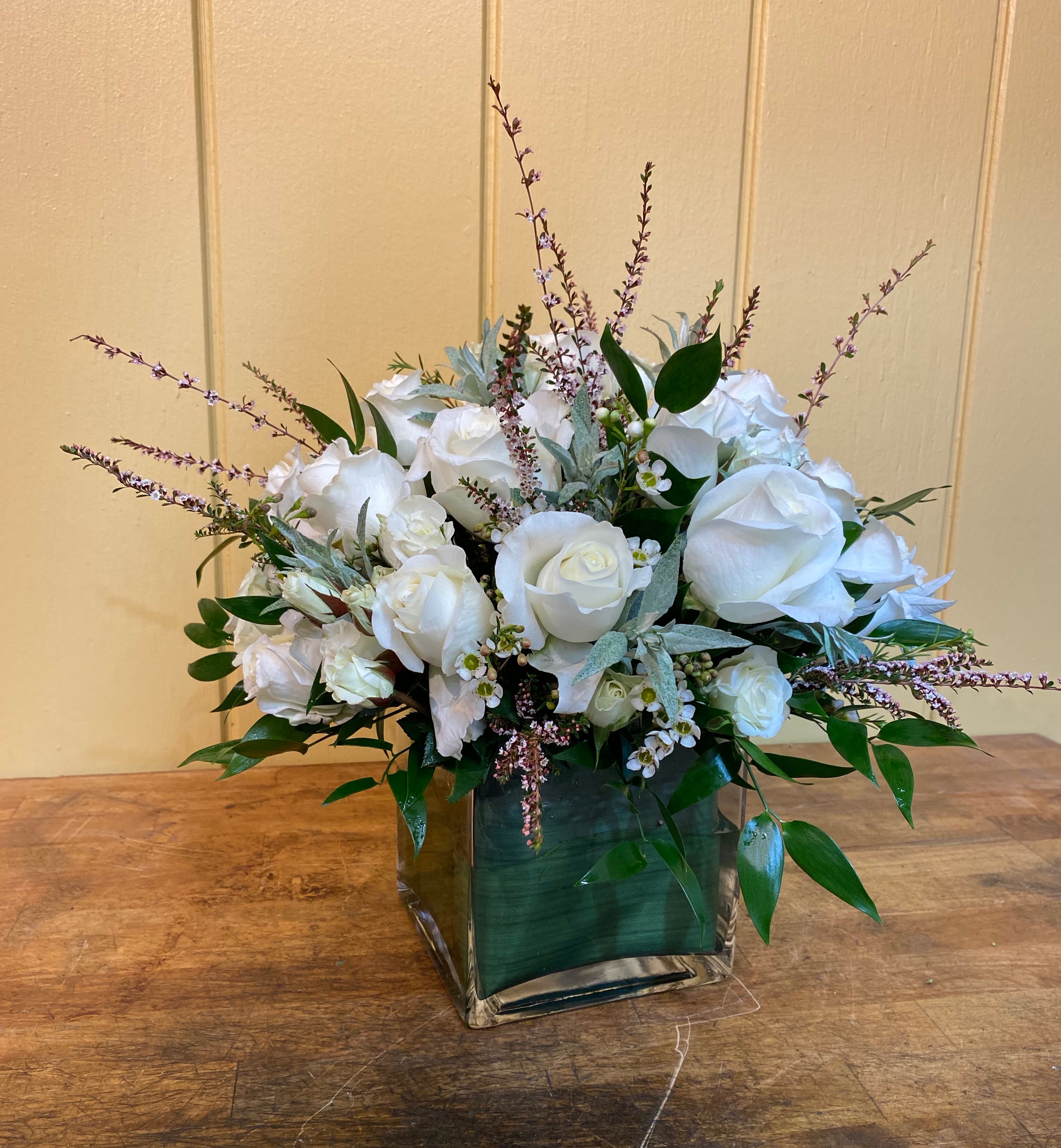 White rose arrangement in a square glass vase with greenery