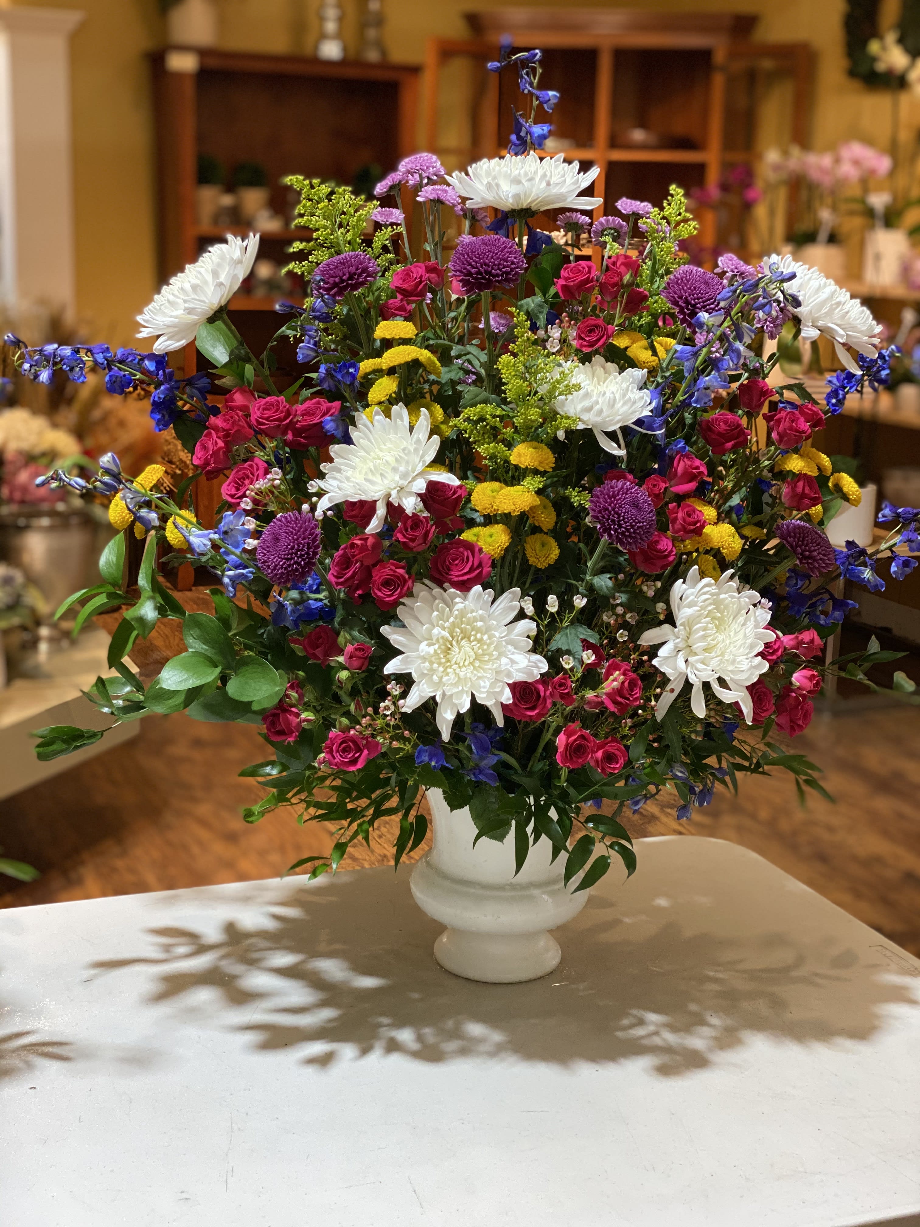 Large mixed flower arrangement in a white vase with pink, white, yellow, and purple blooms.