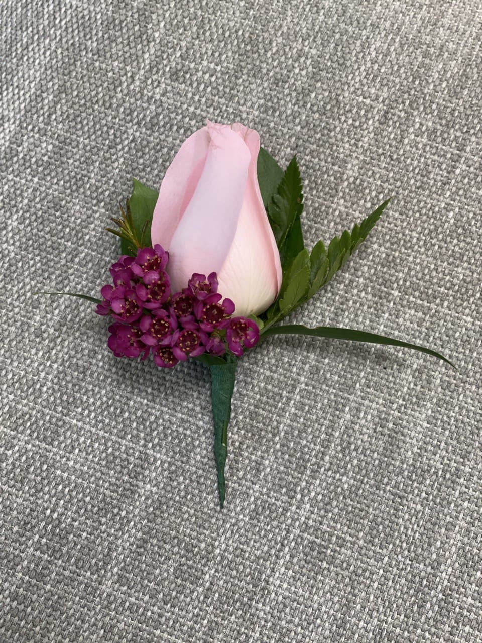 Pink rose boutonniere with small purple accent flowers