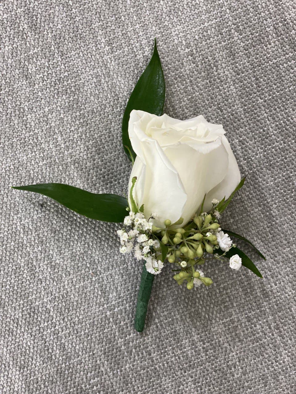 White rose boutonniere with small white filler flowers and green leaves