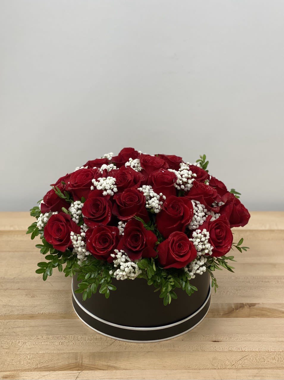 Red roses arranged in a round black box with white filler flowers
