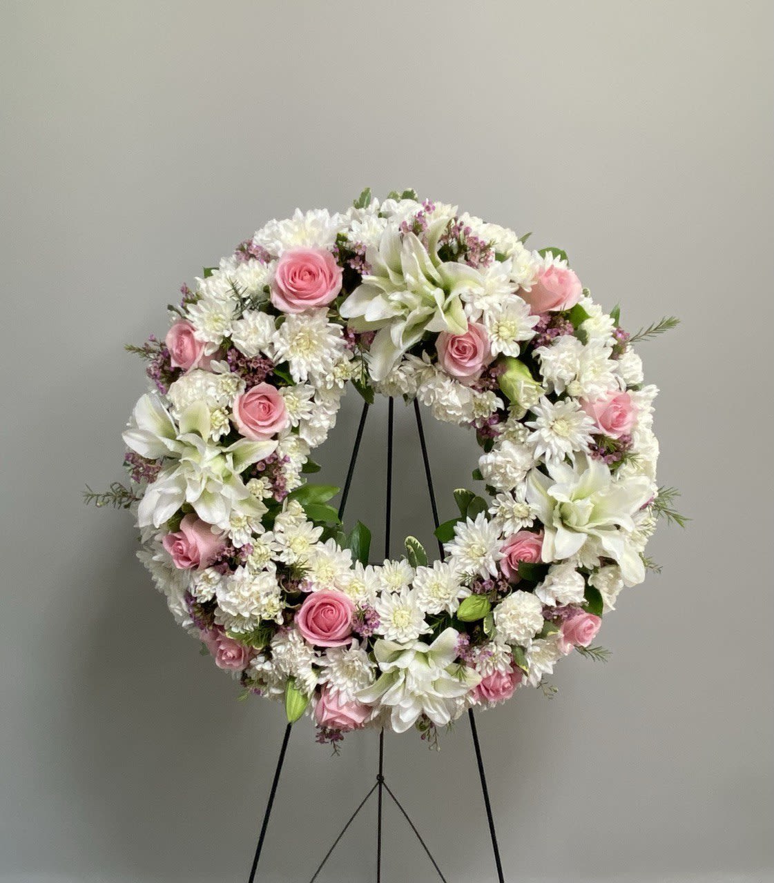 Circular floral wreath with pink roses and white blooms on a black stand