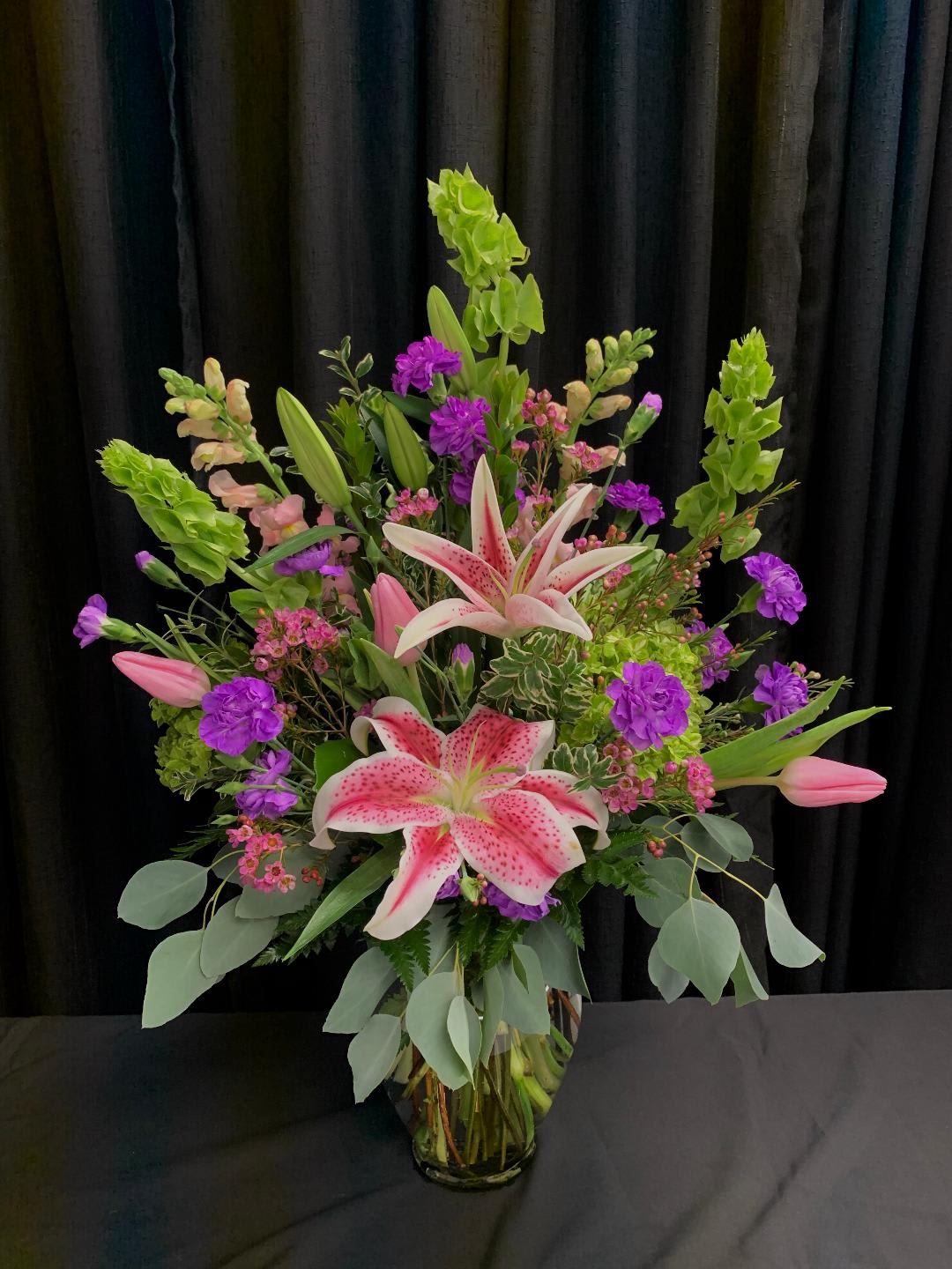 Tall bouquet of pink lilies and purple flowers in a glass vase
