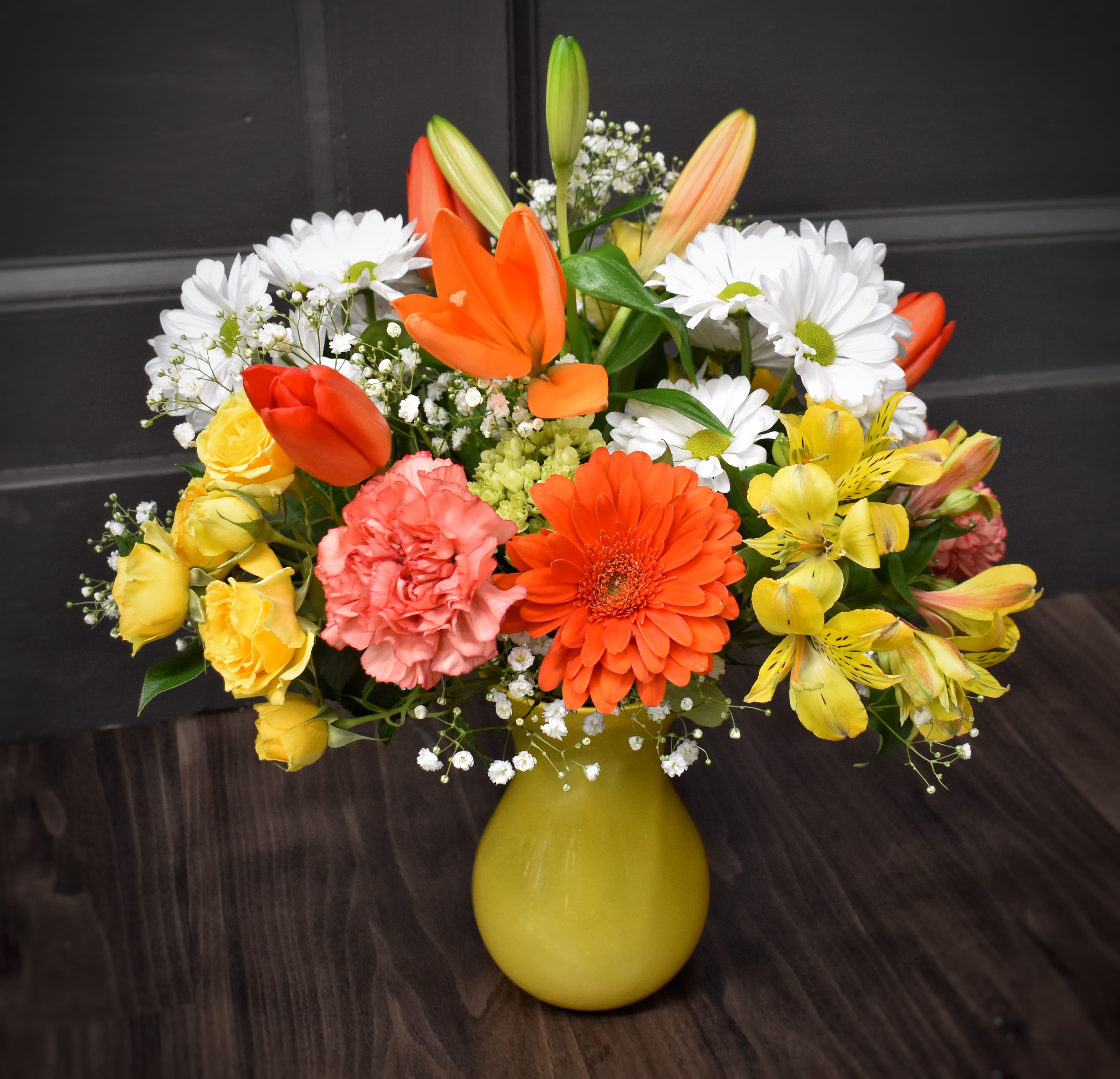 Colorful mixed bouquet in a yellow vase with daisies, roses, and lilies