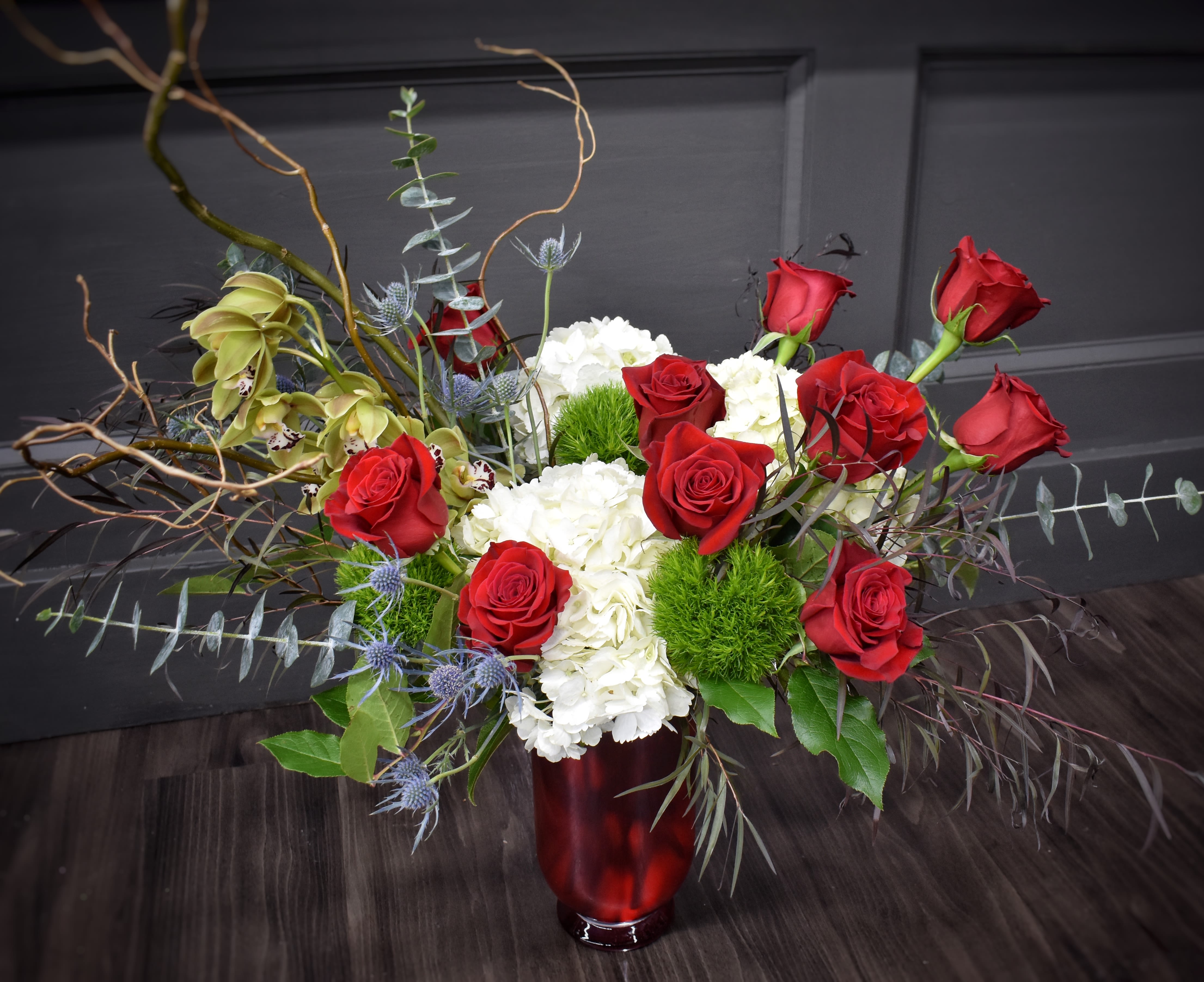 Red roses and white hydrangeas in a red vase with curly branches