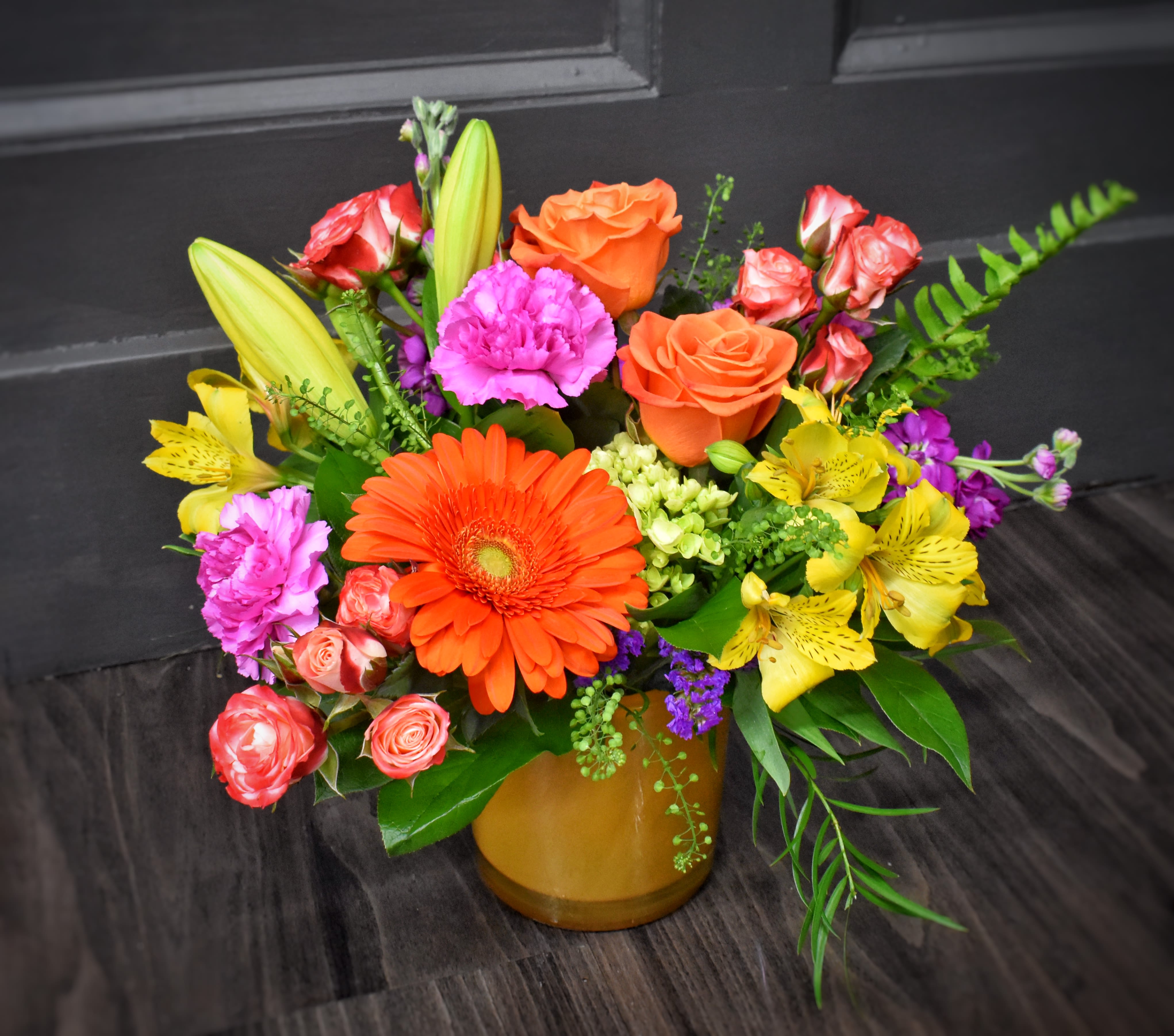 Calypso - Premium - Bright, cheerful blooms in warm oranges and sunny yellows make this mixed-color flower arrangement a joyful pick for a birthday bouquet, congratulations gift, or a "just because" surprise. The rounded design and close layering create an abundant, celebratory feel that will make the person you're thinking of smile the moment it arrives.  Perfect for cheering up a friend, marking a milestone, or brightening a desk or entryway, this premium arrangement reads as both festive and refined. The compact, rounded size fits easily on a table or counter-fresh-cut care is simple: keep water topped up, trim stems every few days, and place away from direct heat to extend vase life.