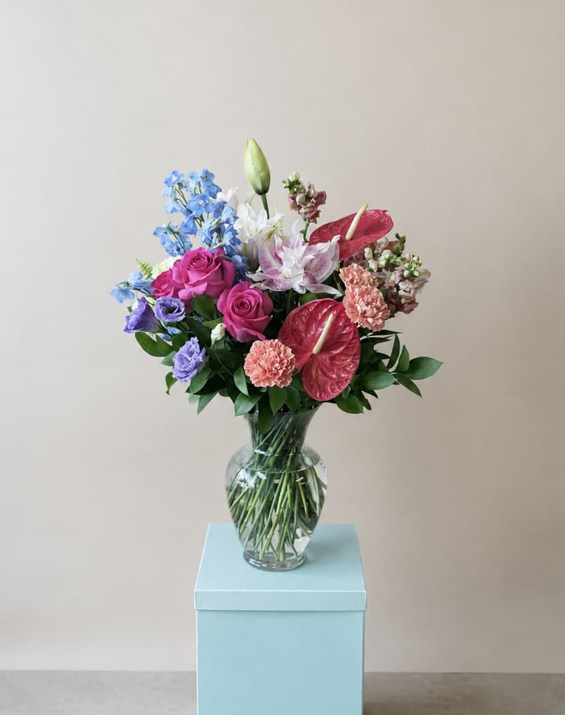 Colorful bouquet in a clear glass vase with roses, lilies, and anthuriums
