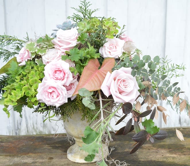 Pink roses and mixed greenery arranged in a stone vase