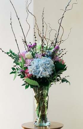 Tall floral arrangement with blue hydrangea in a glass vase