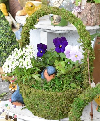 Moss-covered basket with purple and white pansies and small bird figurines