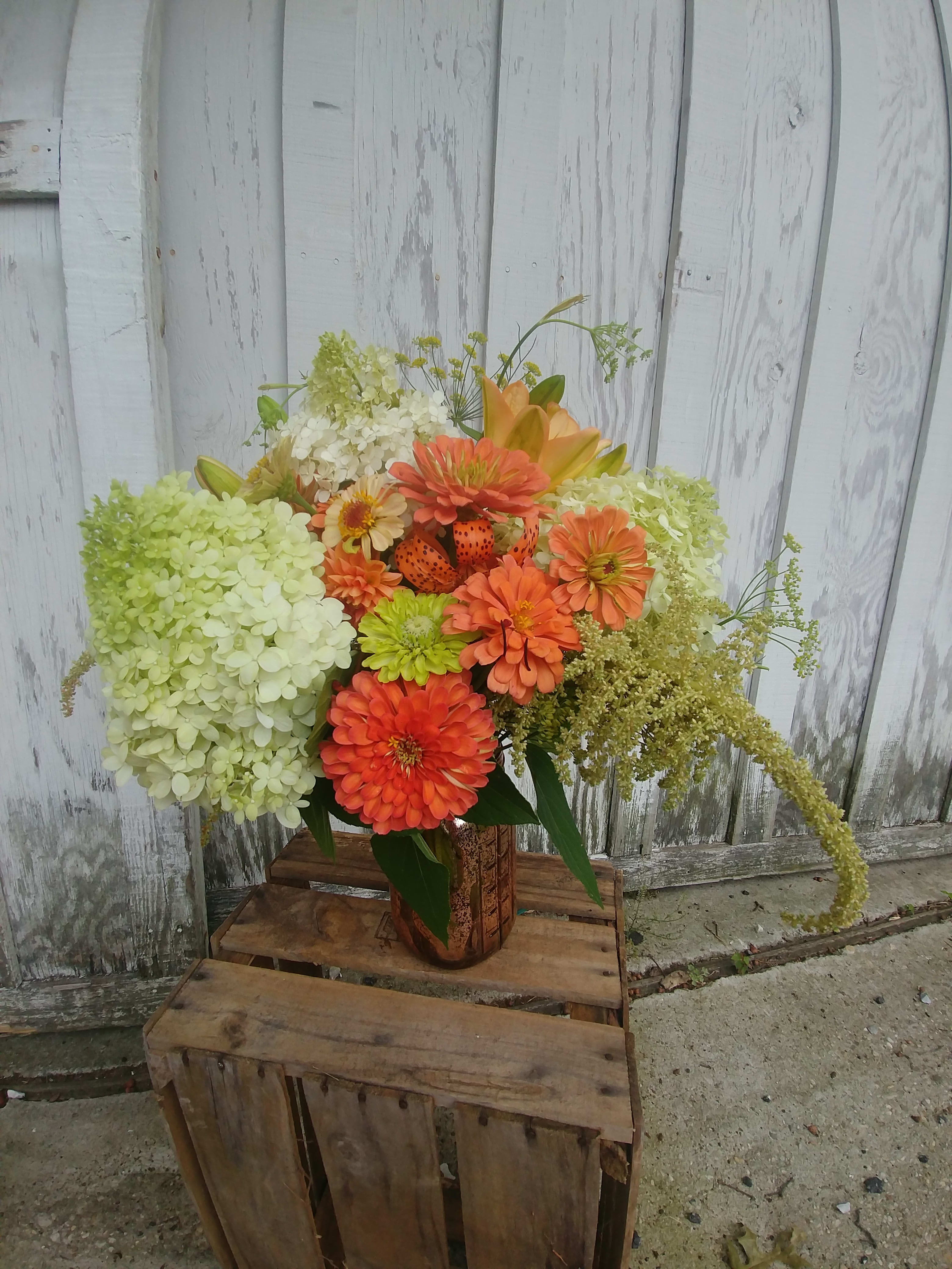 Orange and green floral arrangement in a rustic vase