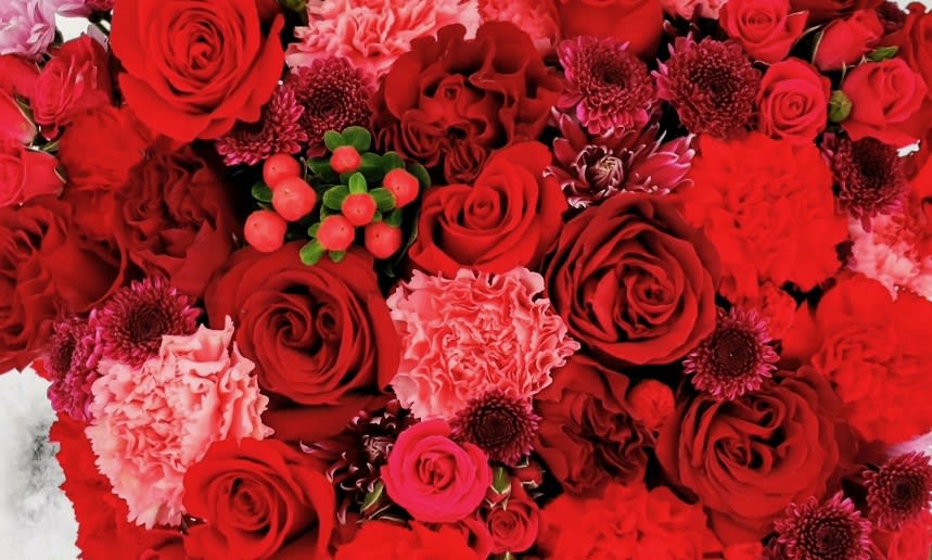 Dense red bouquet with roses, carnations, and small berry accents