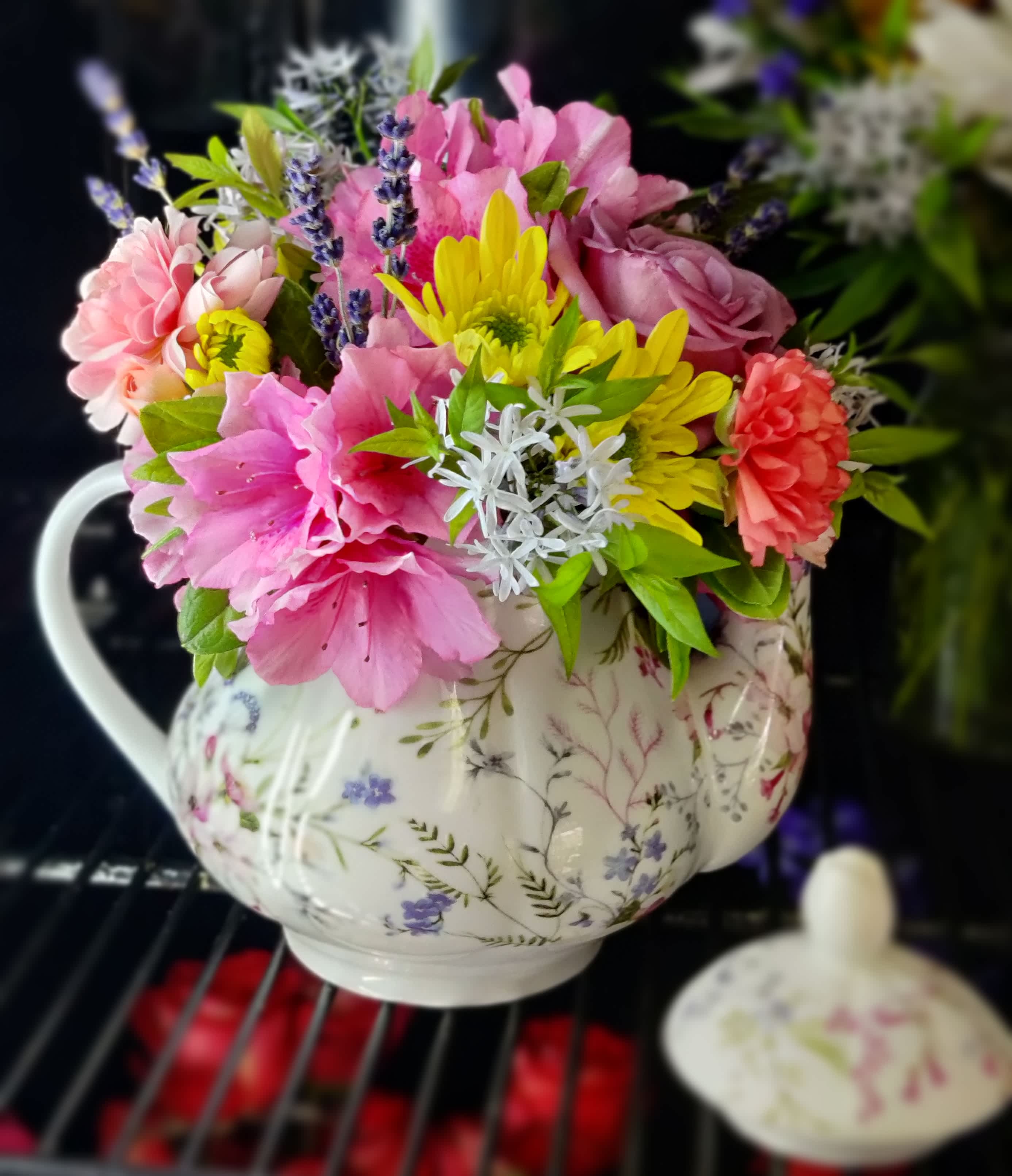 Pink and yellow flowers arranged in a floral teapot vase