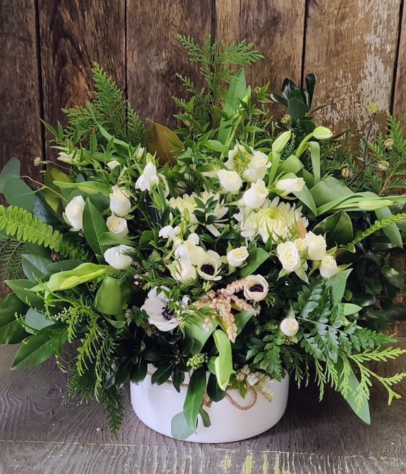 White floral arrangement in a round white box with lush greenery
