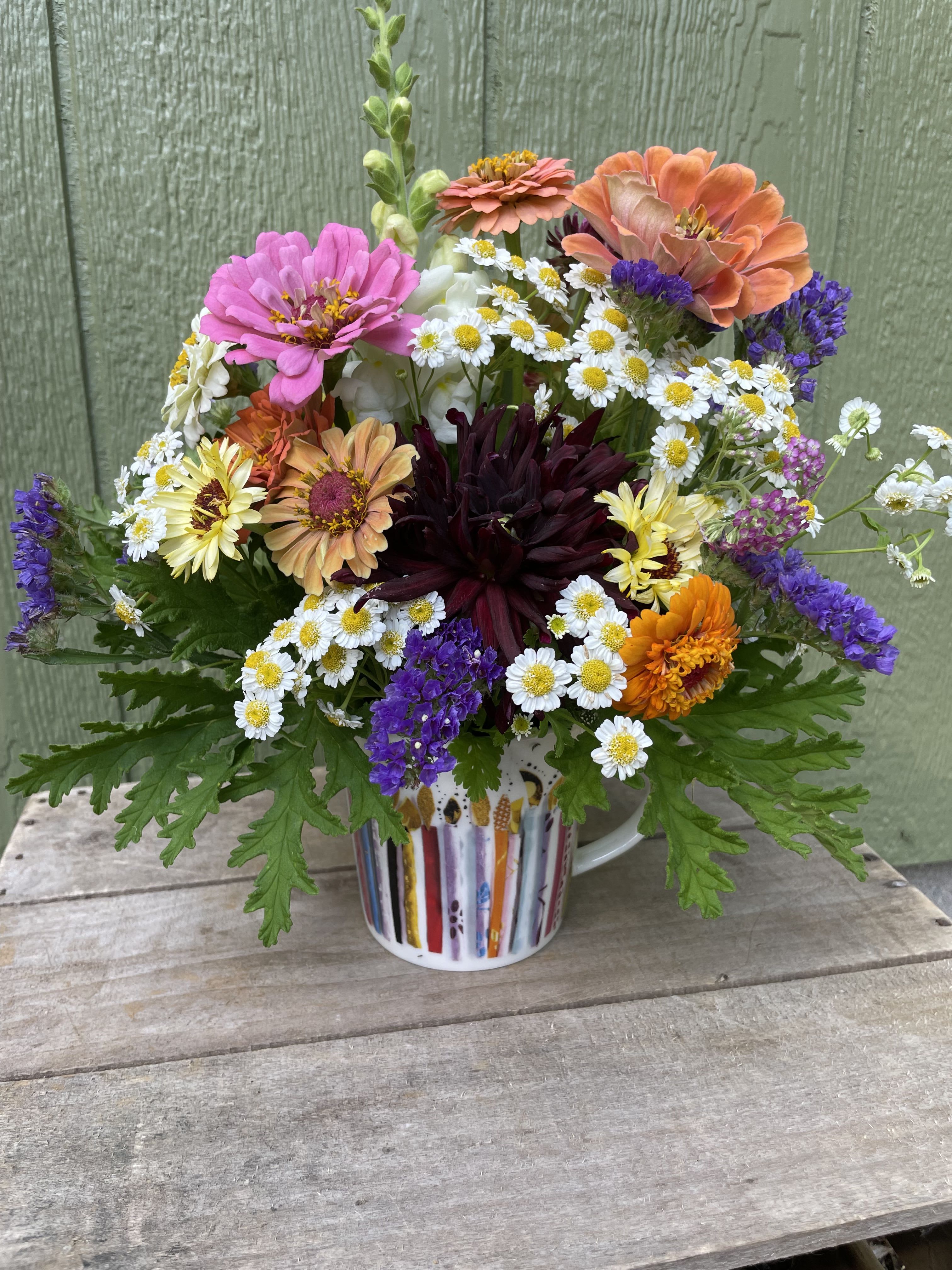 Birthday Mug of Flowers  - A bright, garden-picked mug of flowers that feels like a cheerful morning surprise-perfect as a birthday bouquet. The mixed-color arrangement brings together pinks, purples, sunny yellows, orange accents and fresh greens so the person you're thinking of will feel seen and uplifted the moment they unwrap it.  No special care is required beyond fresh water-place in a cool spot away from direct heat and refresh the water every couple of days to keep blooms looking their best.