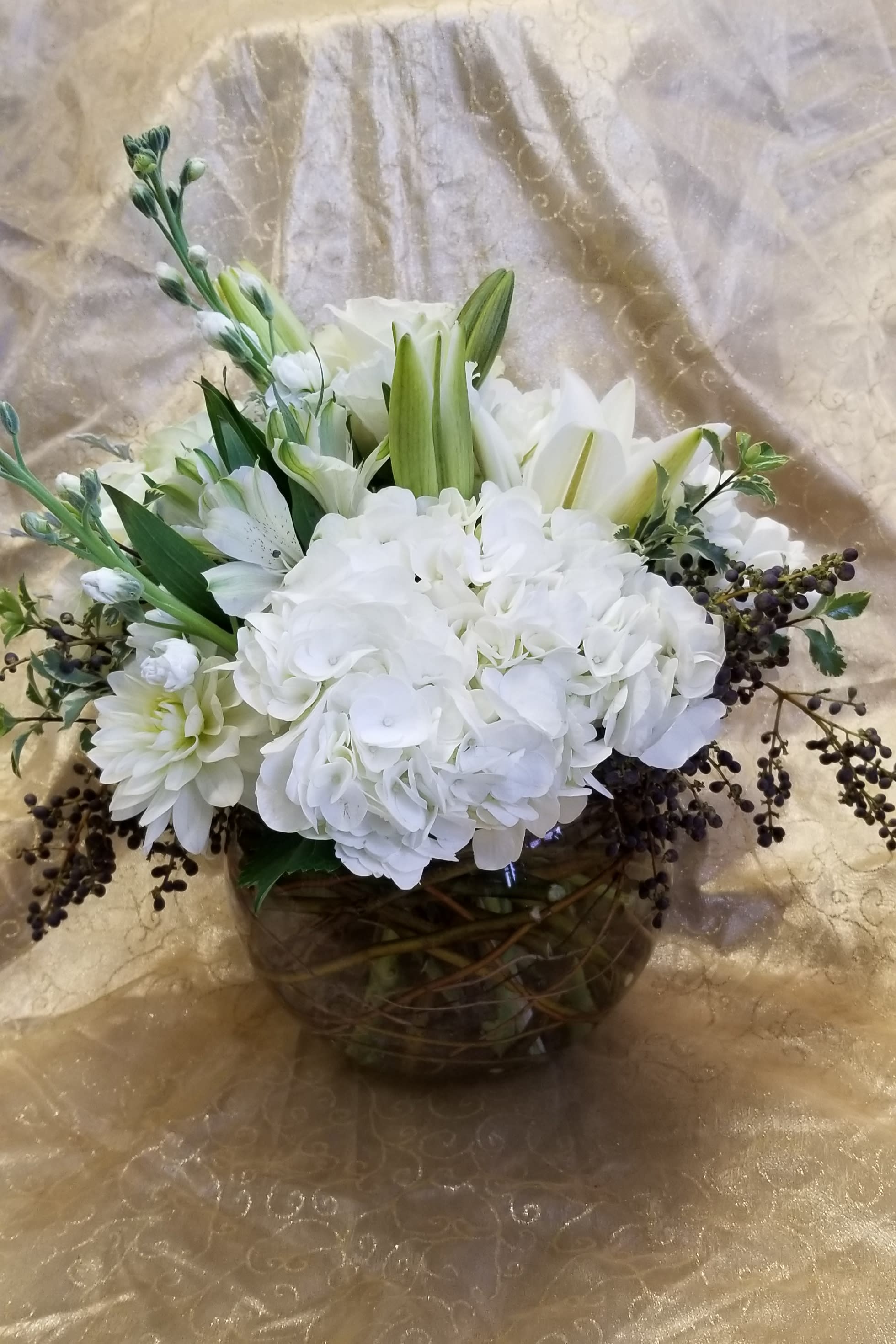 White floral arrangement in a round glass vase with lilies and hydrangeas