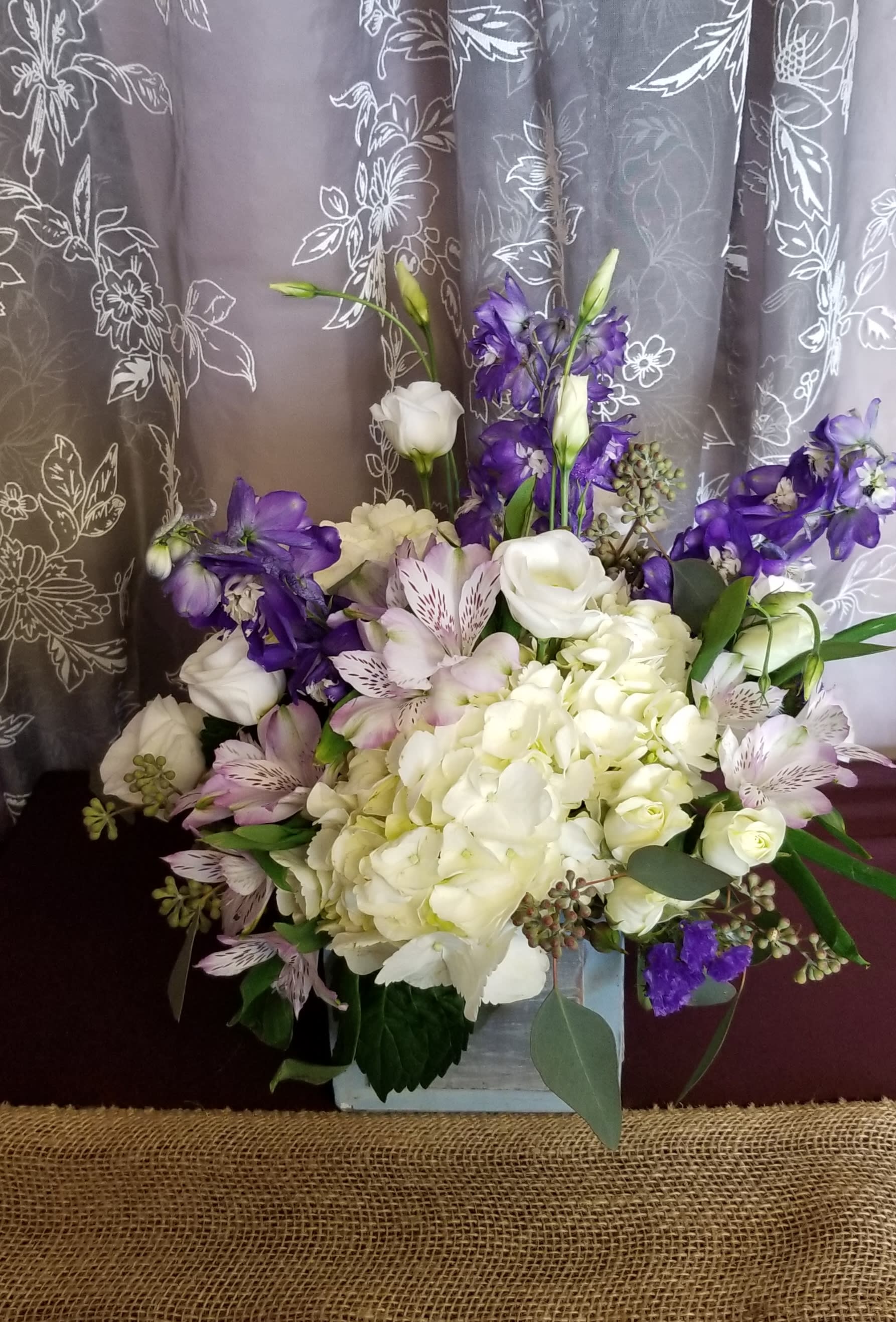 White and purple floral arrangement in a square container