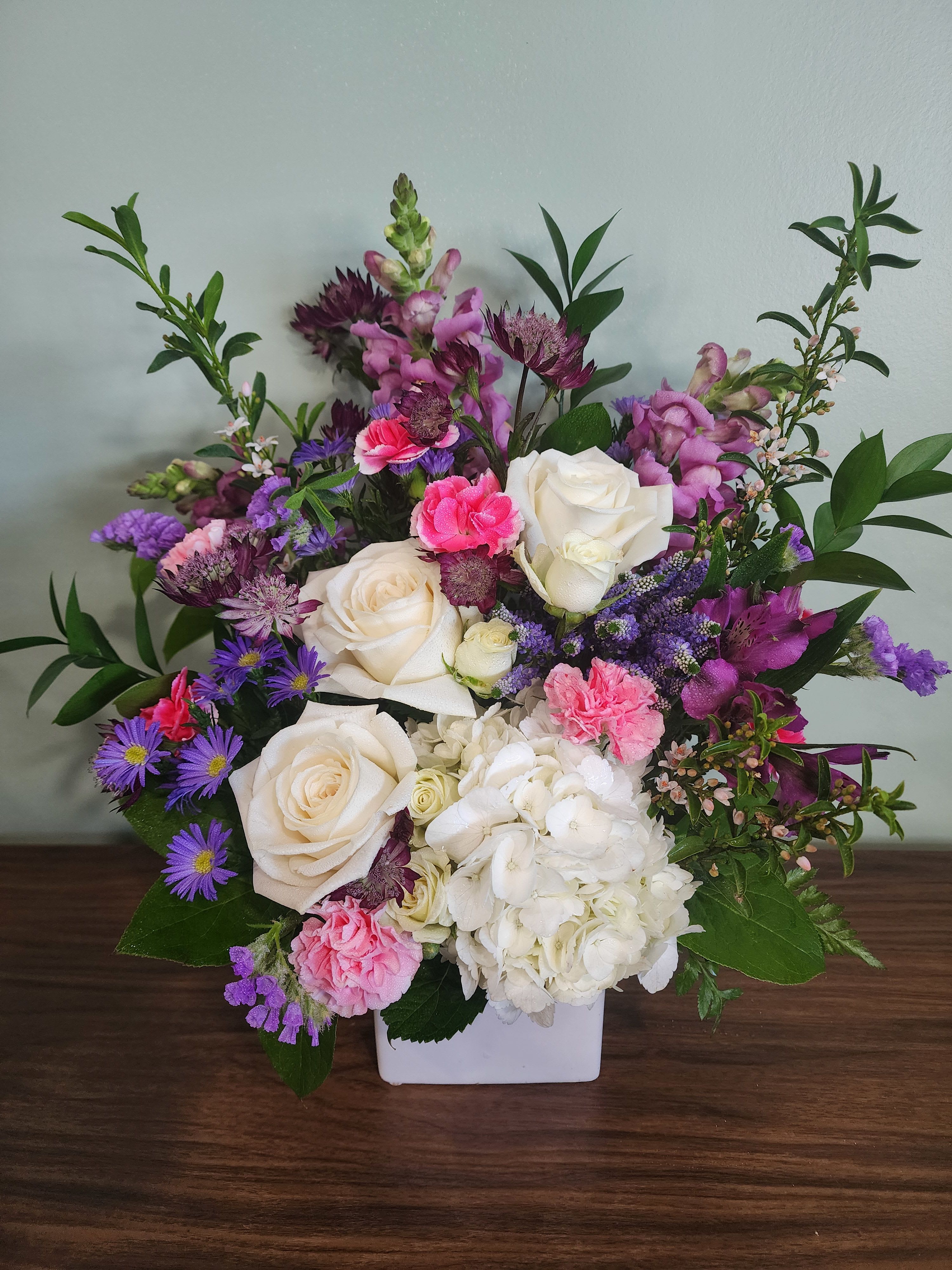 Mixed bouquet of white roses, hydrangea, and pink-purple flowers in a white vase