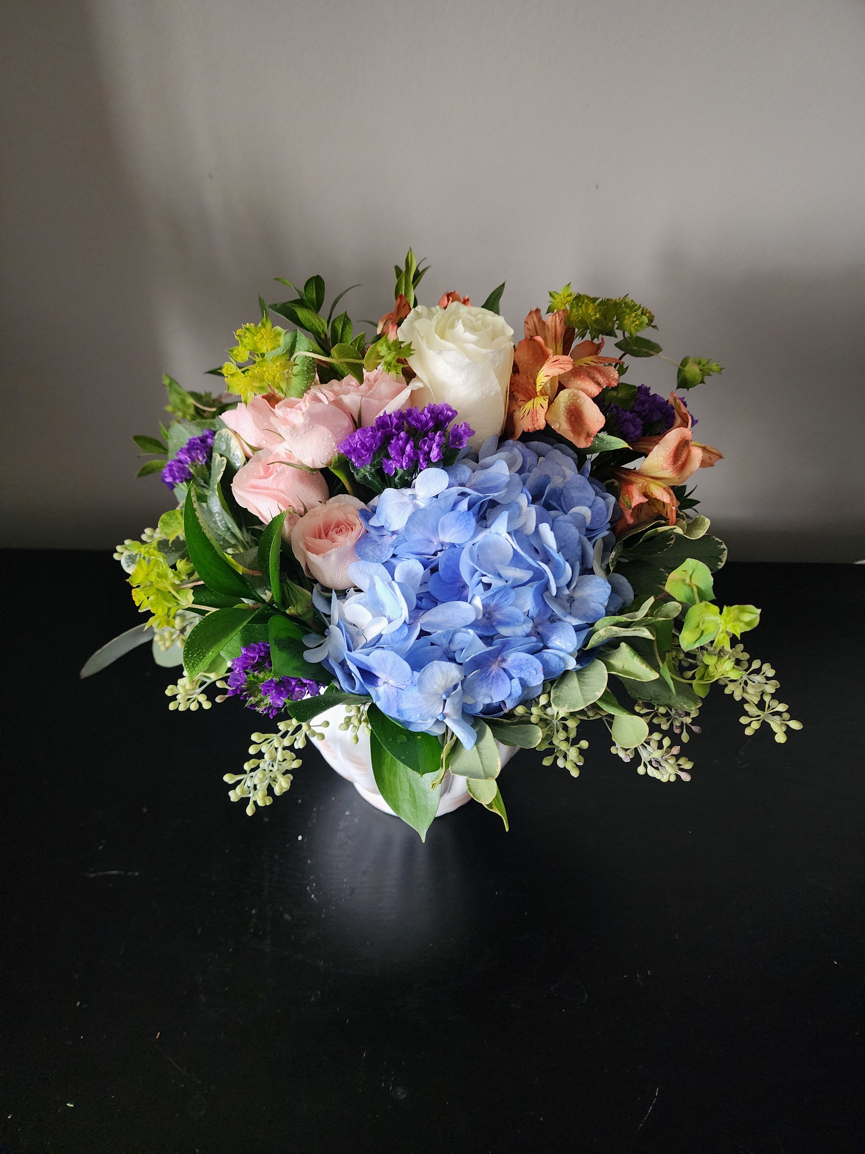 Mixed bouquet with blue hydrangea, pink roses, and white rose in a white vase