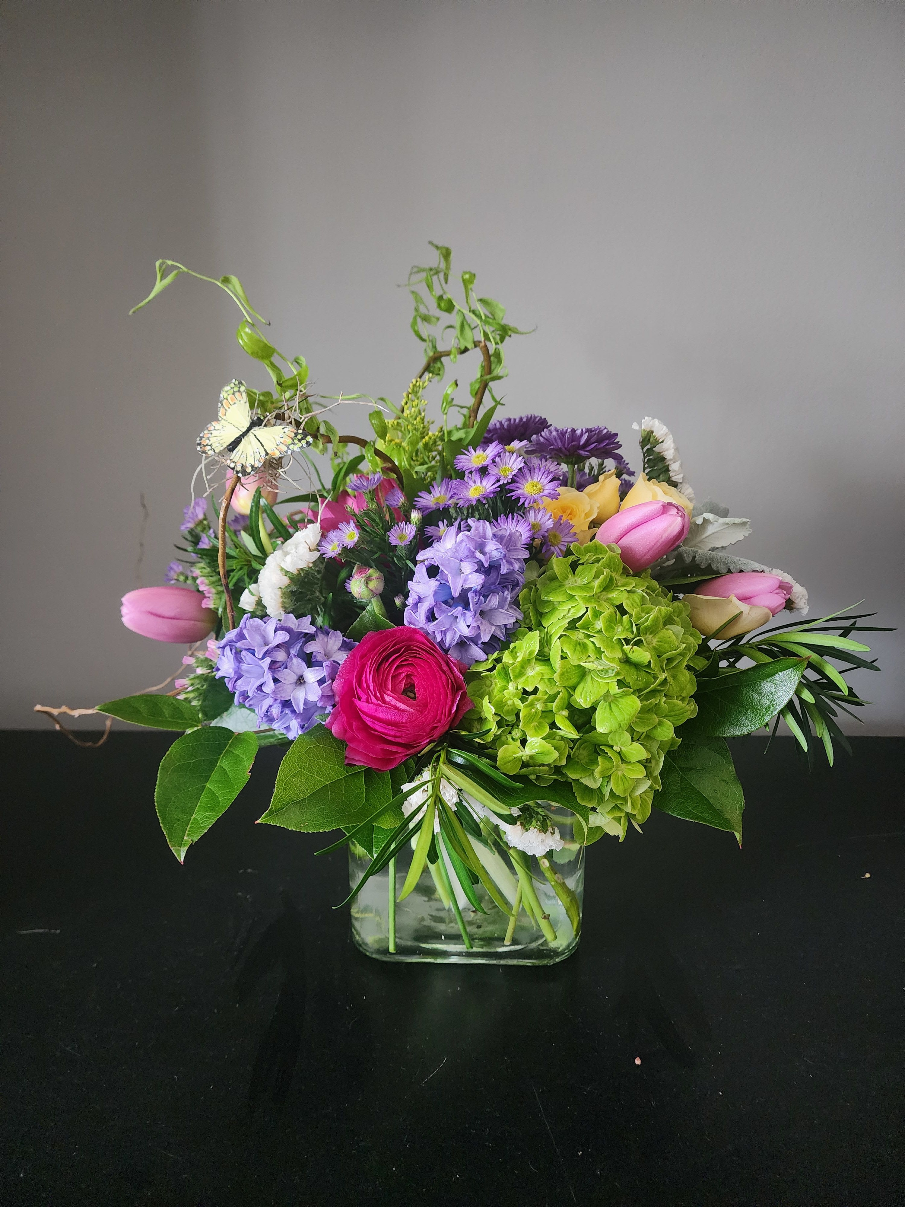 Blushing Garden Luxe by MG Florist  - Blushing Garden Luxe Bouquet  Brighten any occasion with the Blushing Garden Luxe Bouquet, a lush and elegant floral arrangement handcrafted by Magic Garden Florist. Designed with a fresh, garden-inspired style, this stunning bouquet features green hydrangea, soft pink tulips, vibrant hot pink ranunculus, delicate spray roses, fragrant hyacinths, asters, statice, and seasonal greenery.  Arranged in a modern large glass cube vase, this design blends soft blush tones with vivid pinks for a romantic yet contemporary look. Perfect for celebrating life’s special moments or adding a touch of beauty to any home or office, this bouquet is both eye-catching and timeless.  Colors and flowers may vary by availability.   Each arrangement is made fresh to order by our expert florists, ensuring premium quality and long-lasting blooms.  Flower Delivery in Rochester, NY  Looking for flower delivery in Rochester, NY.  The Magic Garden Florist proudly offers reliable, same-day and next-day flower delivery in Rochester and surrounding areas. Whether you're sending birthday flowers, anniversary blooms, or a thoughtful surprise, this bouquet is a perfect choice for local delivery.  We specialize in Rochester, NY floral arrangements designed with care, creativity, and the freshest flowers available.