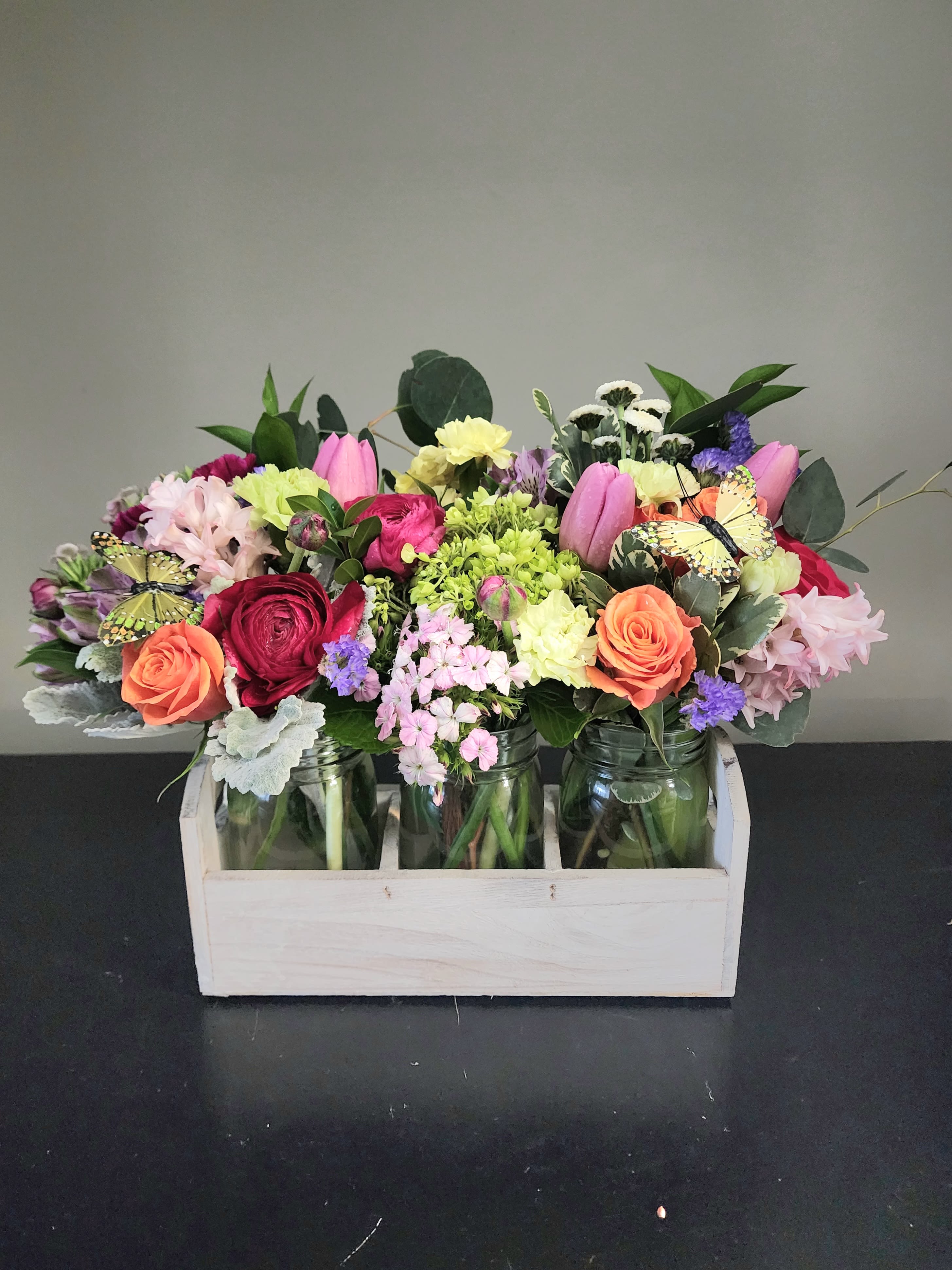 Colorful mixed flower arrangement in mason jars inside a light wooden crate