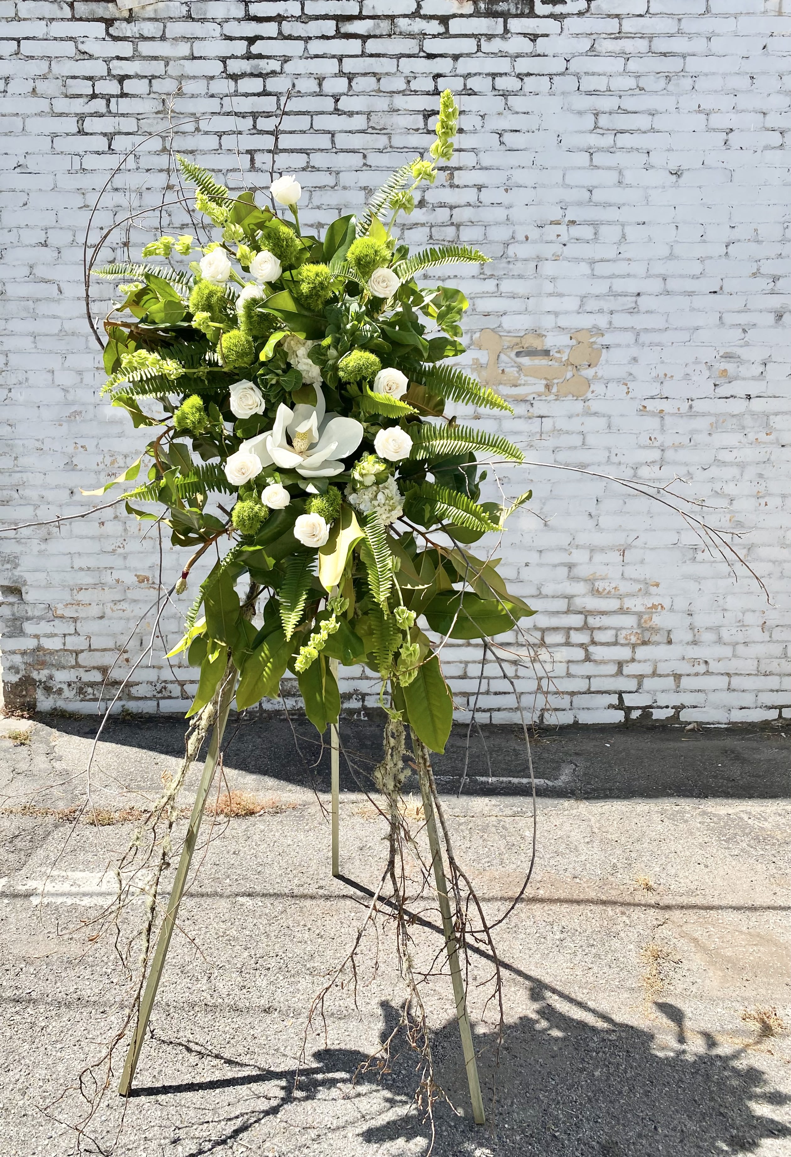 Tall white and green floral standing arrangement on a tripod easel