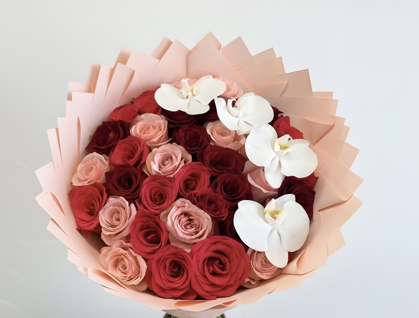 Bouquet of red and blush roses with white orchids in pale pink wrap
