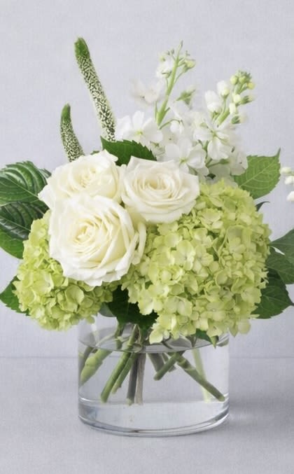 White roses and pale green hydrangeas in a clear glass vase