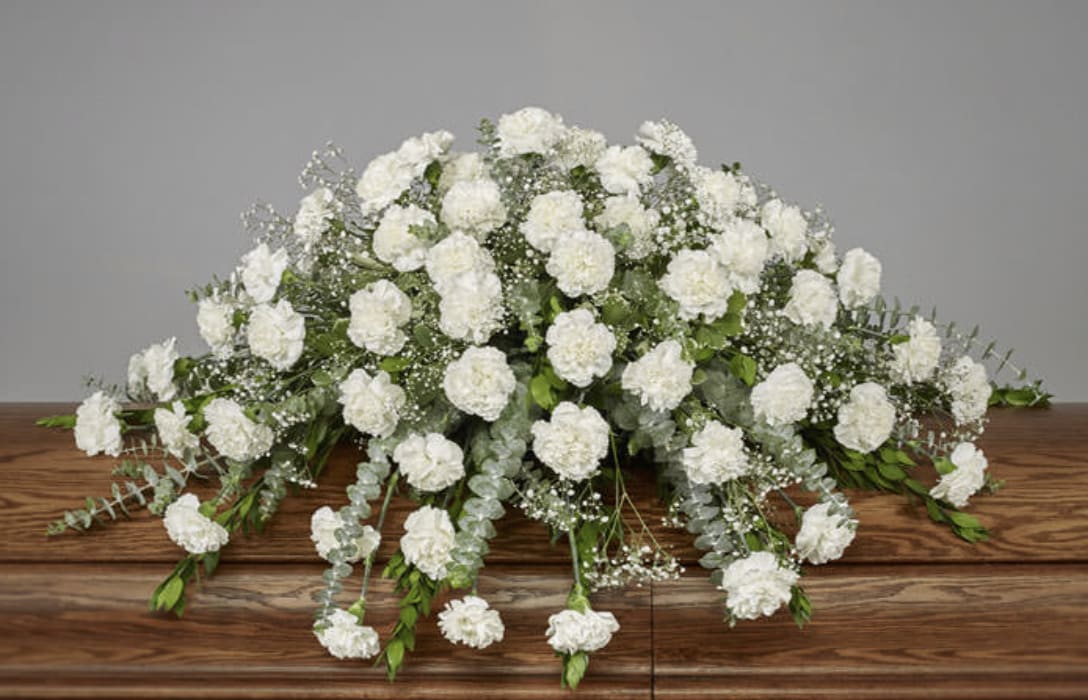 Large white carnation spray on a wooden casket