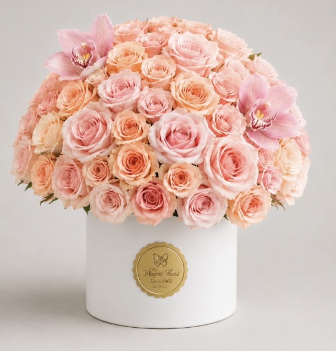 Pink and peach roses arranged in a white hat box with two pink orchids