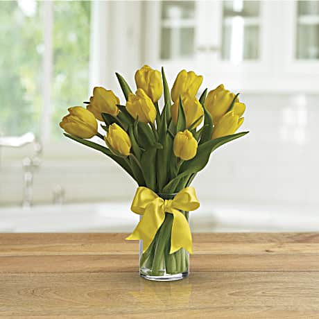 Yellow tulips in a clear glass vase tied with a yellow ribbon.