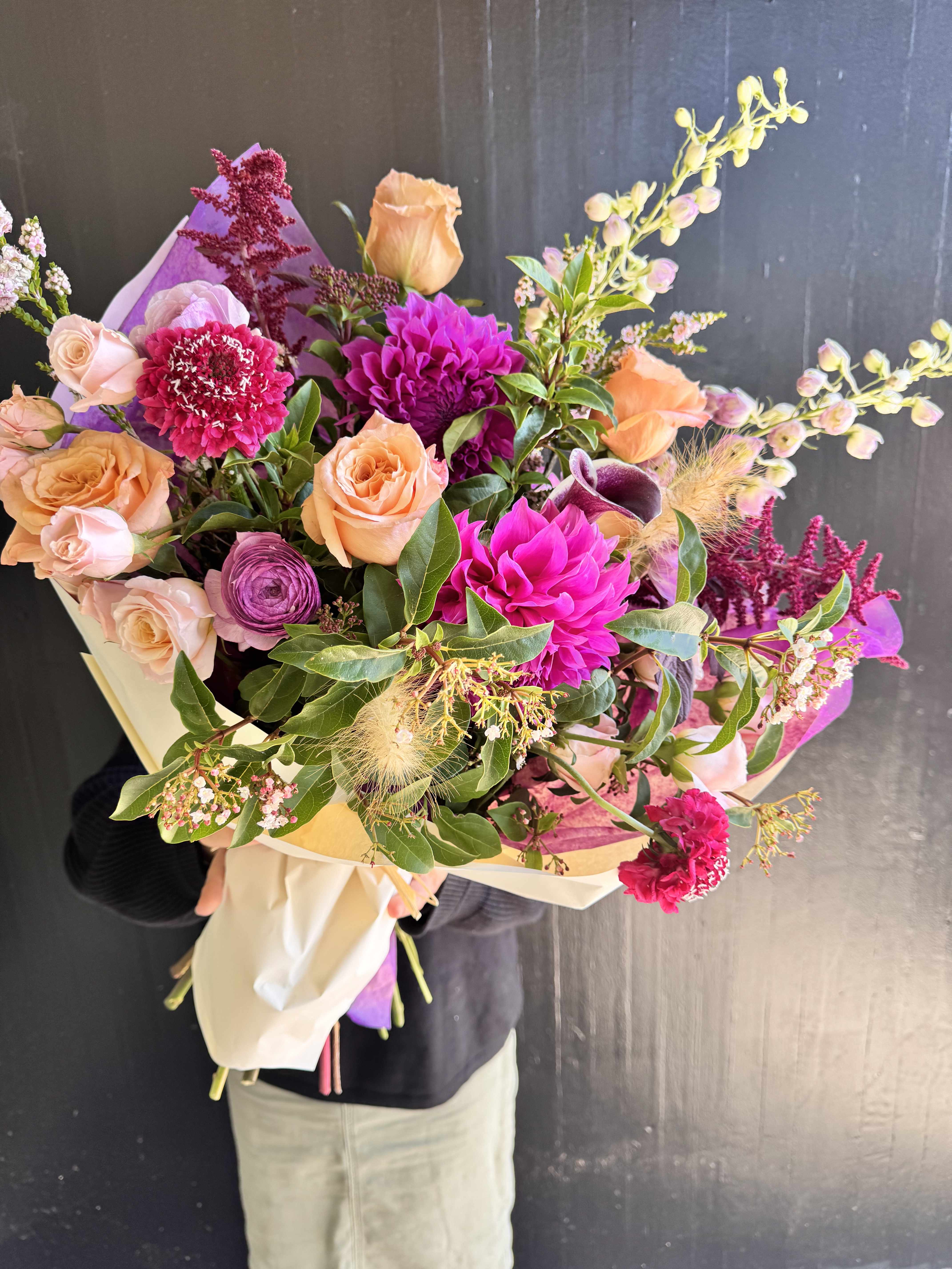 Hand-tied bouquet of peach and magenta flowers wrapped in paper