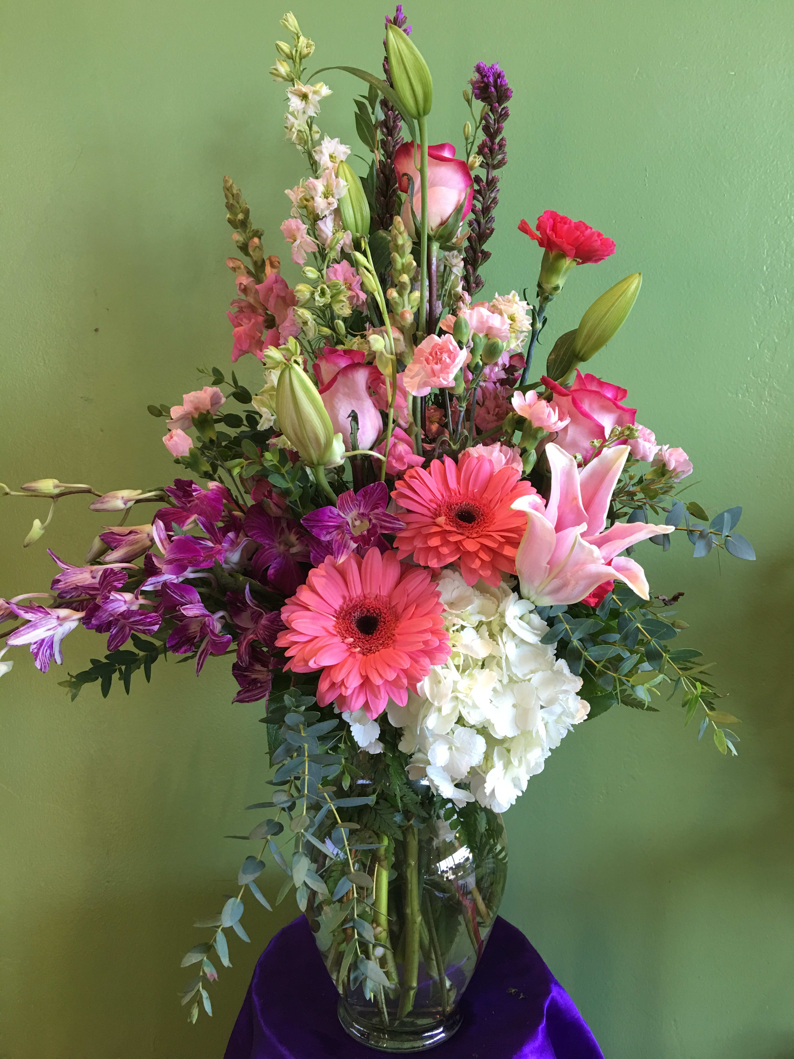 Tall mixed bouquet with pink lilies, gerbera daisies, orchids, and white hydrangea in a glass vase
