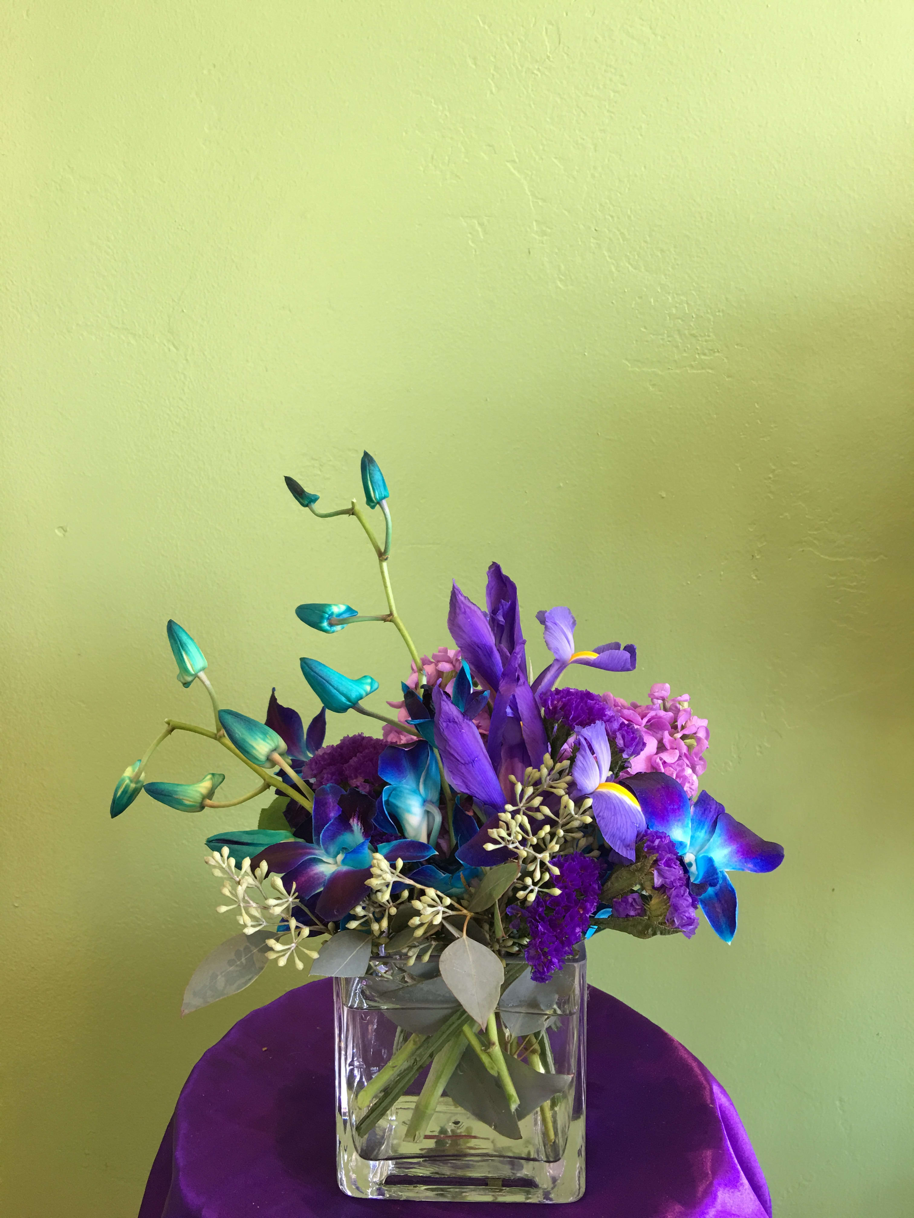 Purple and blue floral arrangement in a clear square vase
