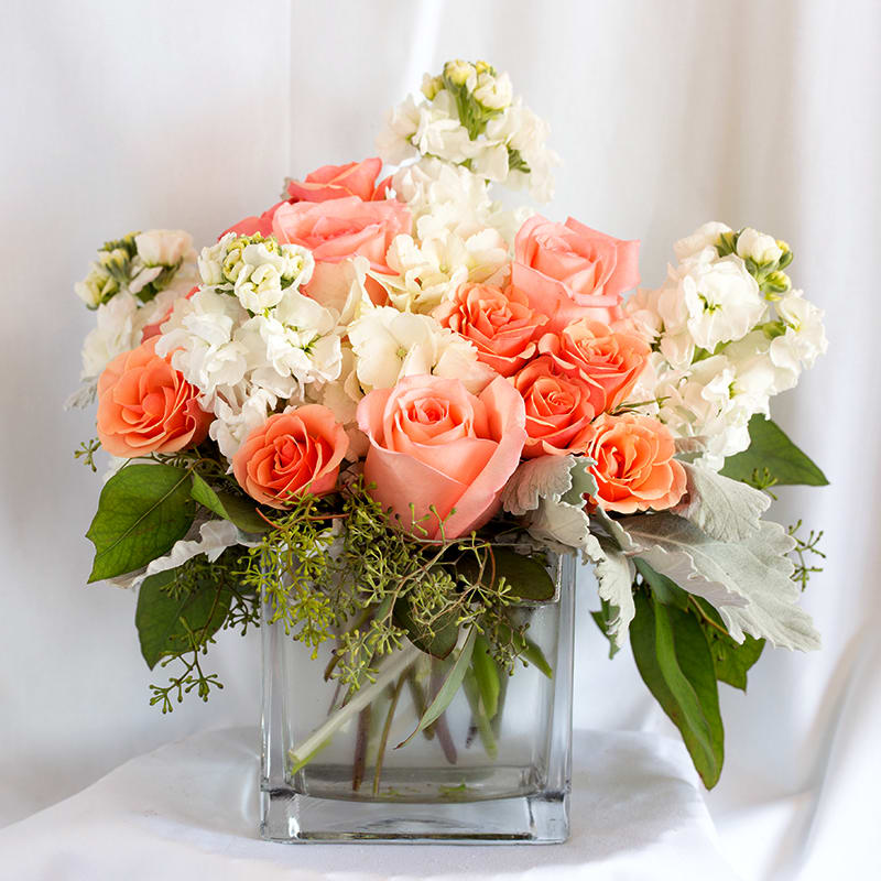Peach and white roses arranged in a clear glass vase