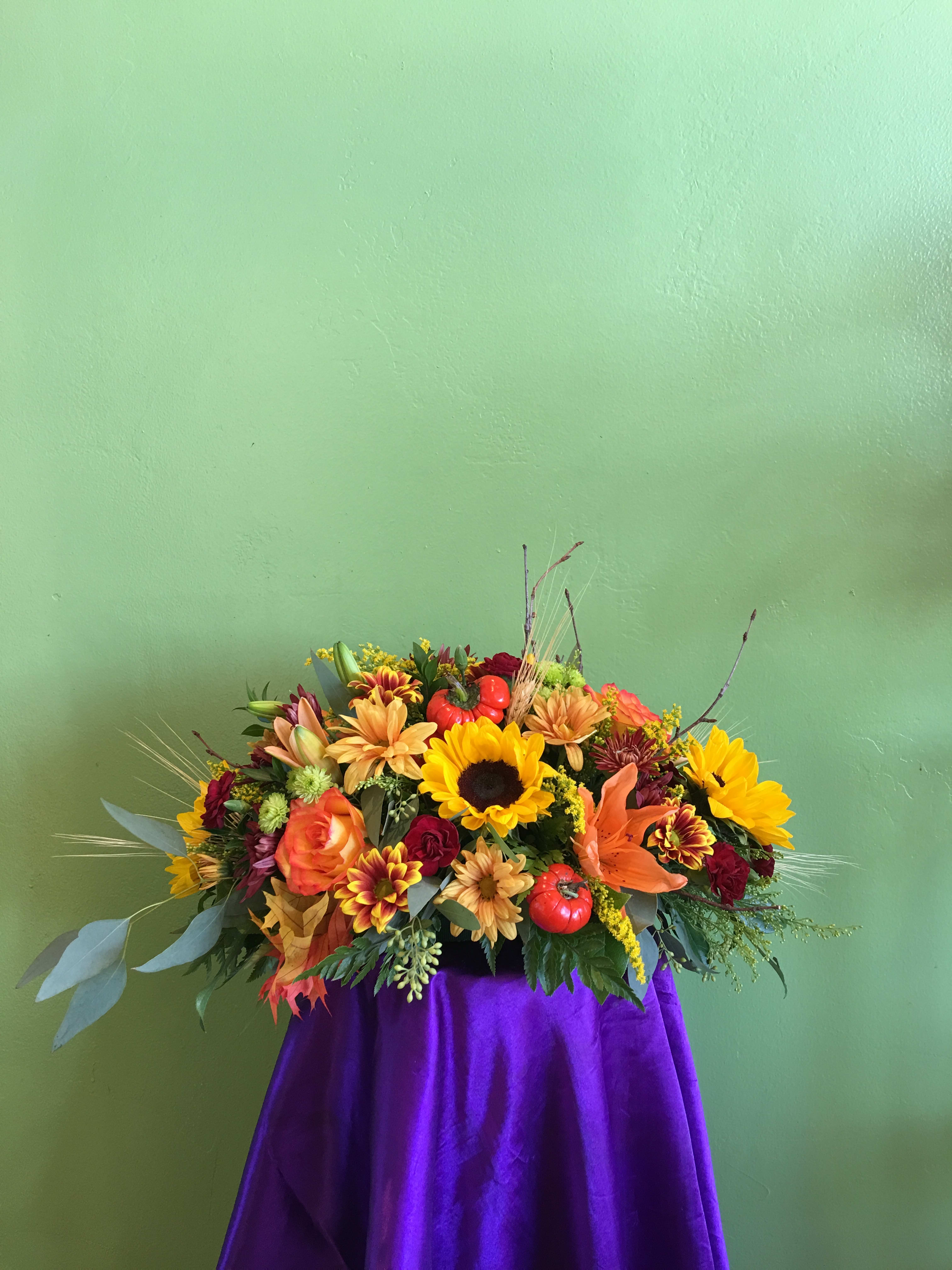 Autumn floral arrangement with sunflowers, lilies, and roses on a purple drape
