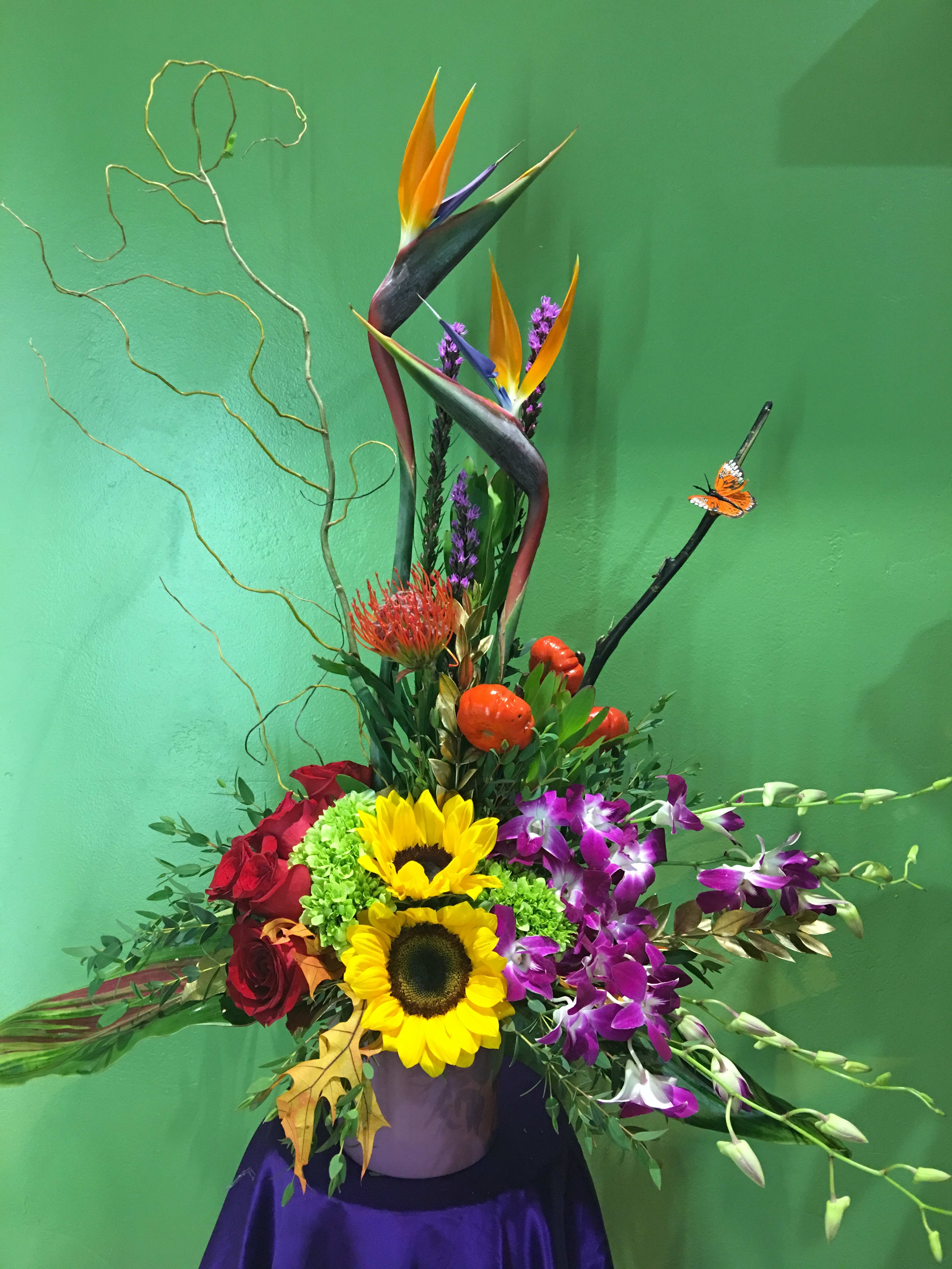 Tropical flower arrangement with sunflowers, orchids, and red roses in a vase